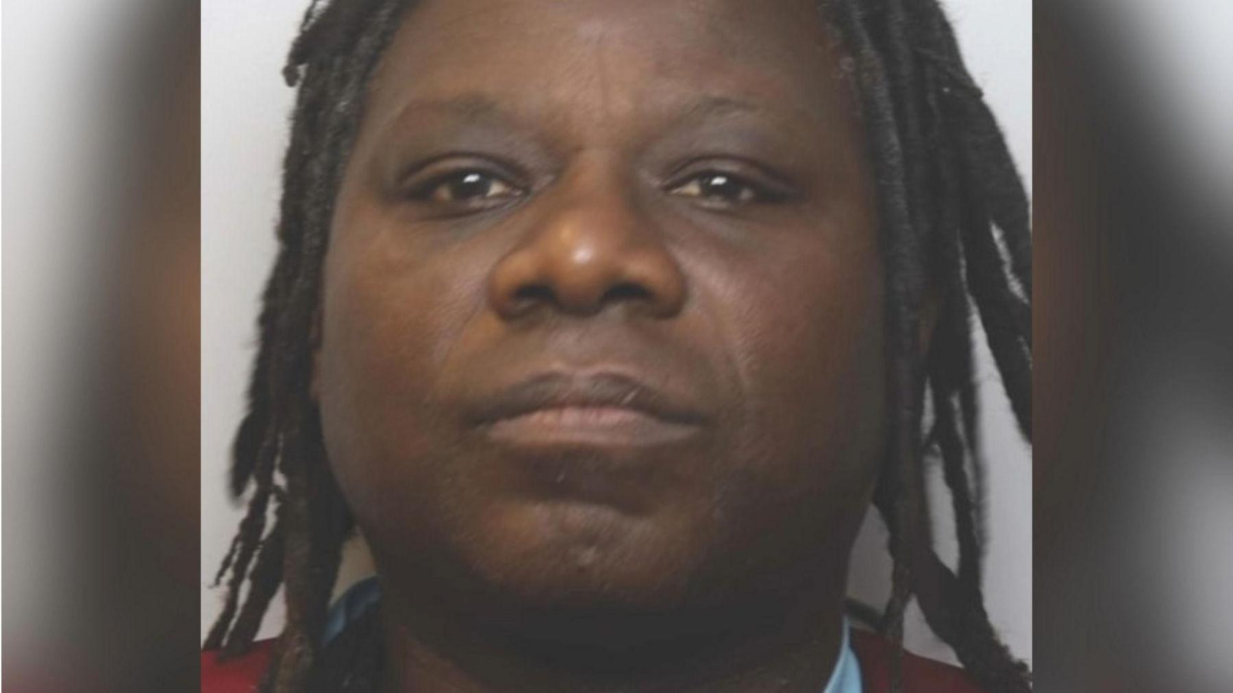 A police mugshot of William Kyaruhanga. He had dreadlocks and is standing against a pale white backdrop.