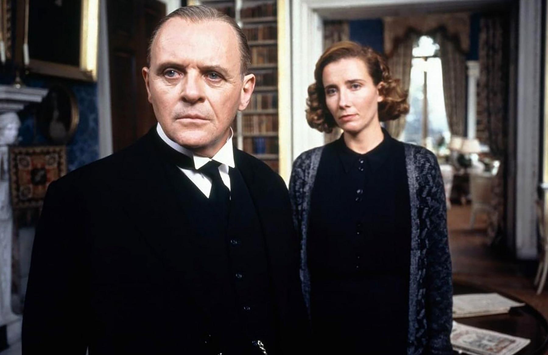 Sir Anthony in the foreground, unsmiling, in black suit and tie and waist coat
as the buttoned-up butler Stevens and Dame Emma Thompson as Miss Kenton -- in black blouse and blue loose cardigan, brown hair, parlty curled in The Remains of the Day. They are in the study, with book shelves in the background