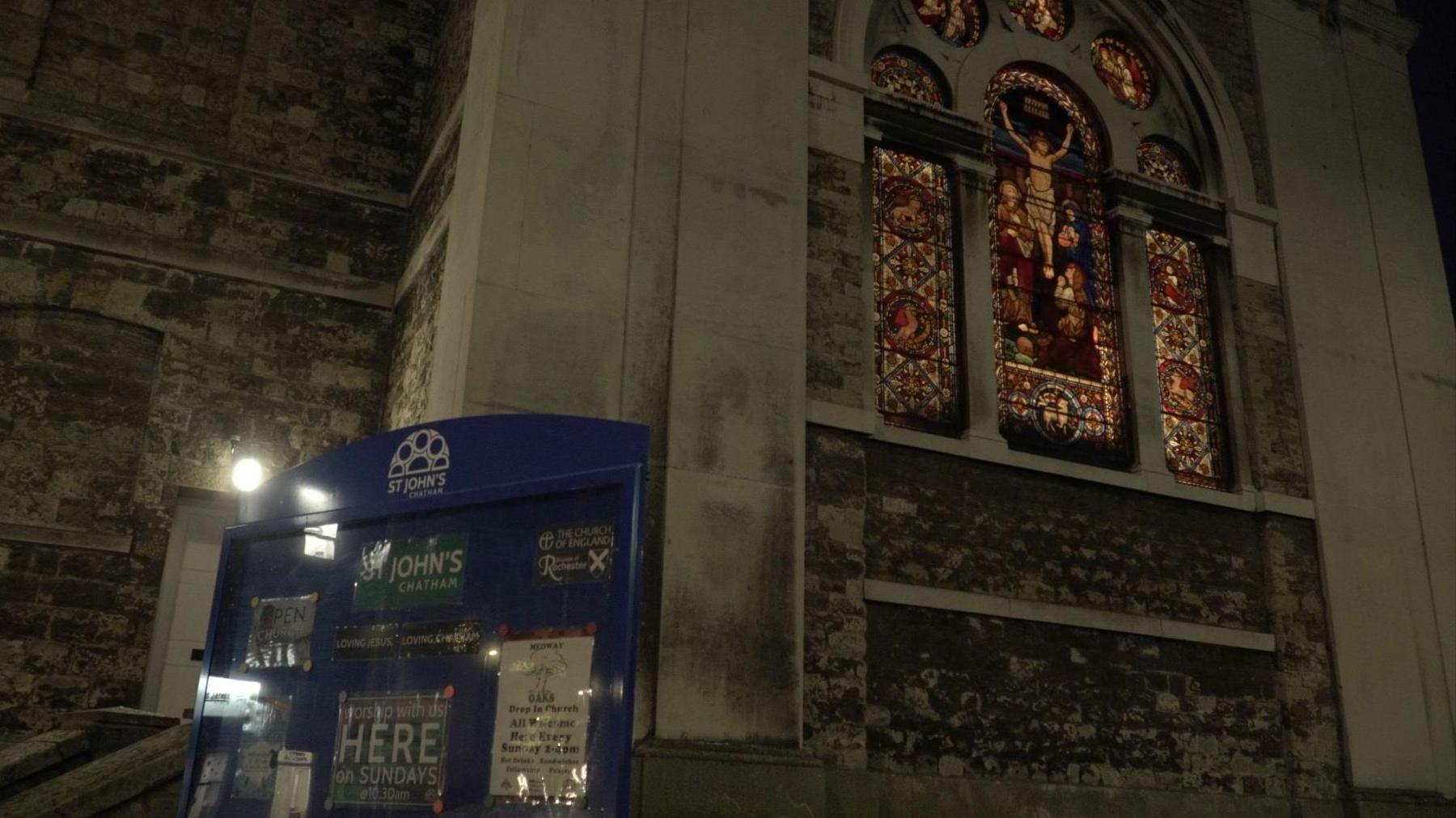 The outside of St John's church in Chatham, Kent. A stained-glass window can be seen in the image alongside an advertising board for the church. 