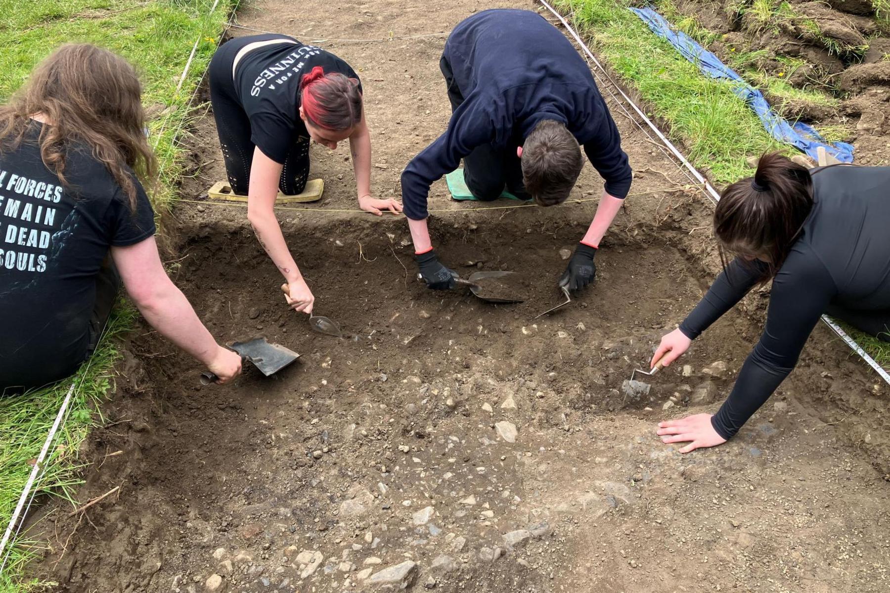 Four people use trowels to carefully clear away soil in an area excavated at the garden festival site.