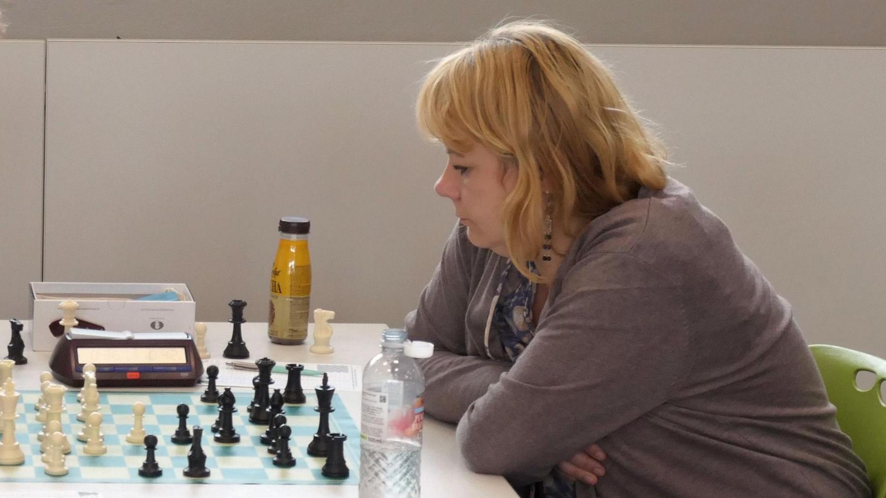 Kata Toma, sat at a chess board playing black with bottles of water on the table and a timing clock