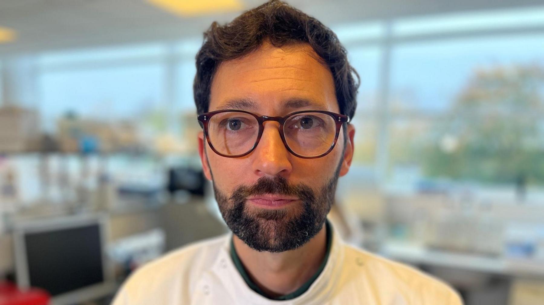 Prof Daniel Streicker has a dark beard, dark hair and dark glasses. He is in a science lab.