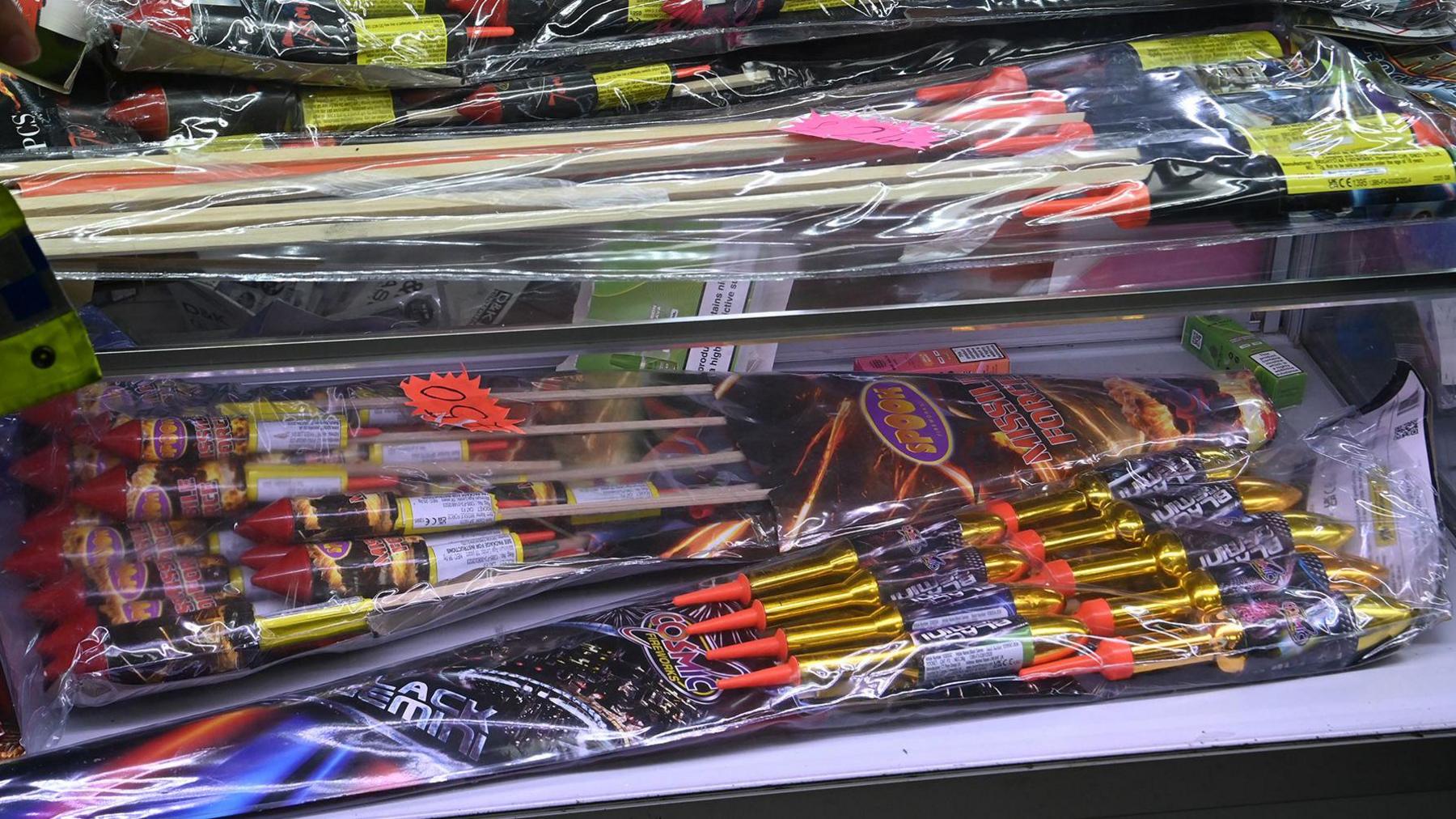 Two shelves full of packets of rocket-style fireworks in clear plastic packaging.
