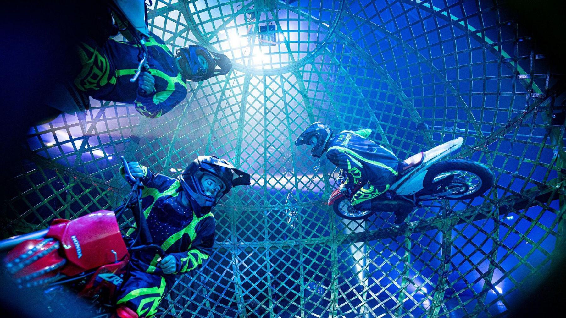 Three motorcyclists ride around inside a giant wheel as they rehearse for performances at Circus Vegas on the Downs in Bristol. They are wearing illuminated patches on their motorbike leathers and are lit up by spotlights