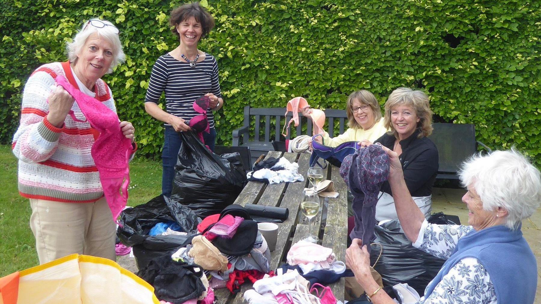 Five women sorting through a selection of donated bras on a garden bench.