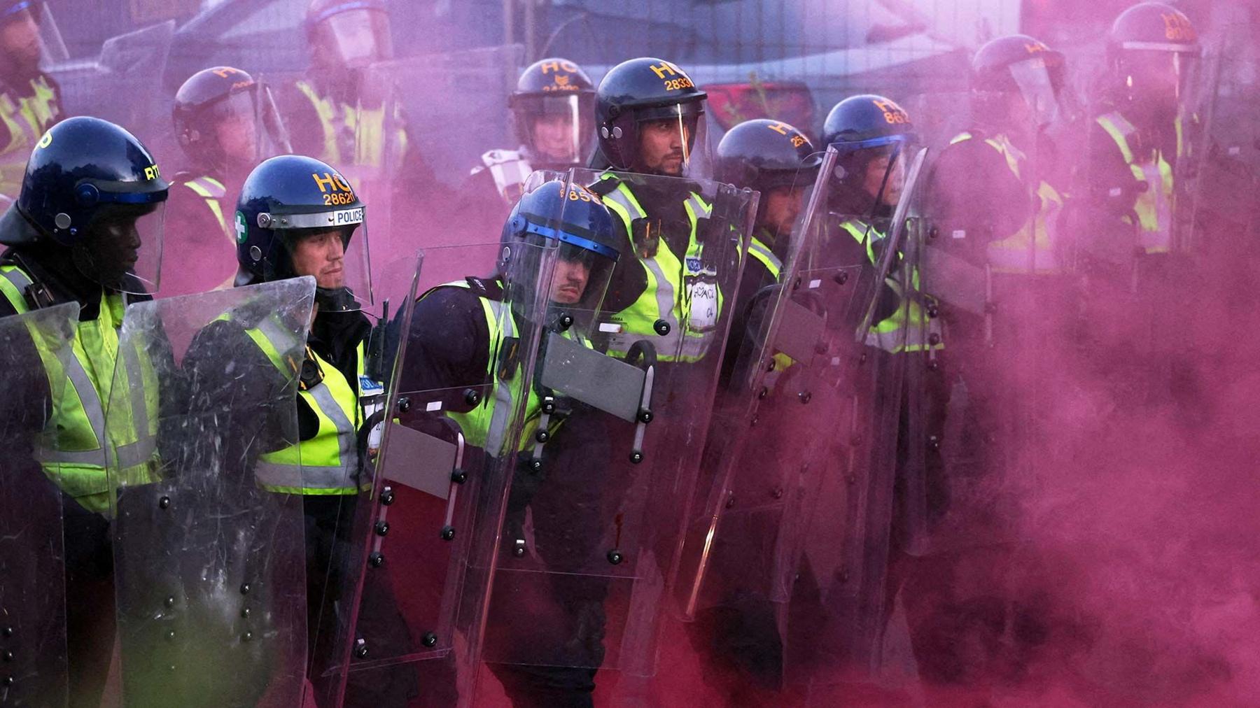 Police officers stand guard amid dark pink colored smoke during a demonstration in Southampton, June 2, 2026. 