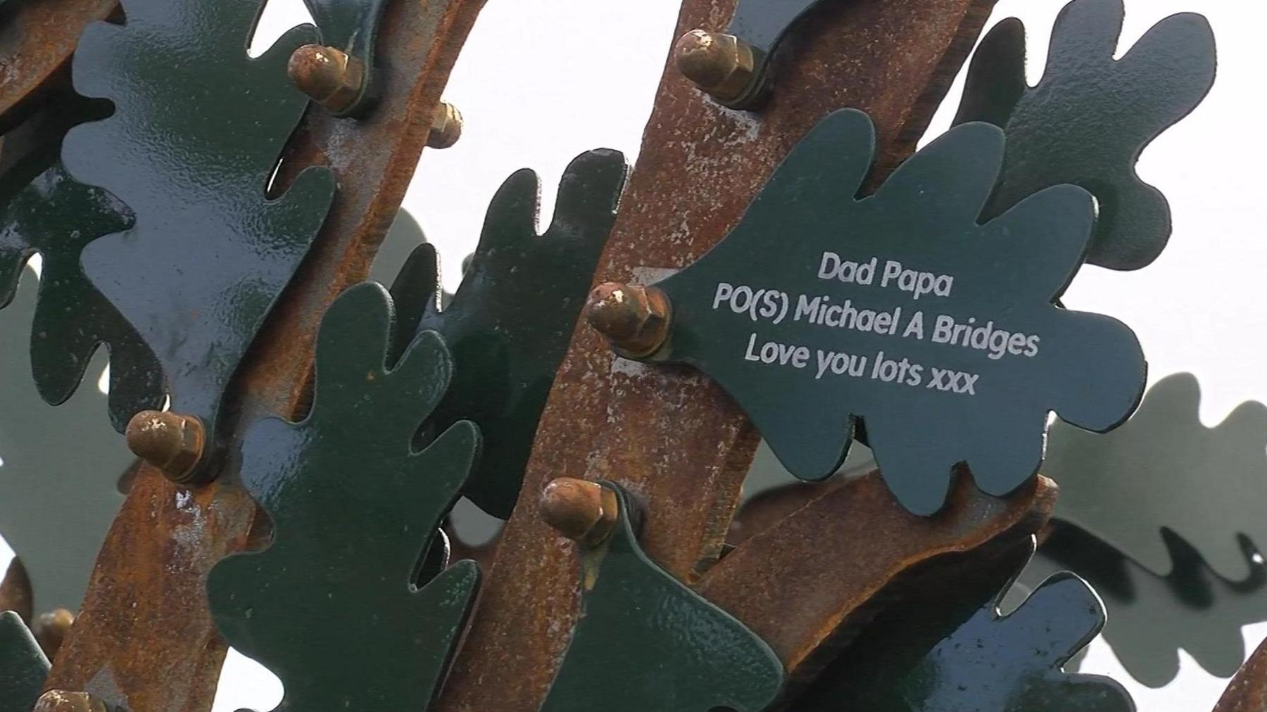 A close up of the metal leaves and branches on the tree. One reads: 'Dad Papa PO(S) Michael A Bridges Love you lots xxx'.