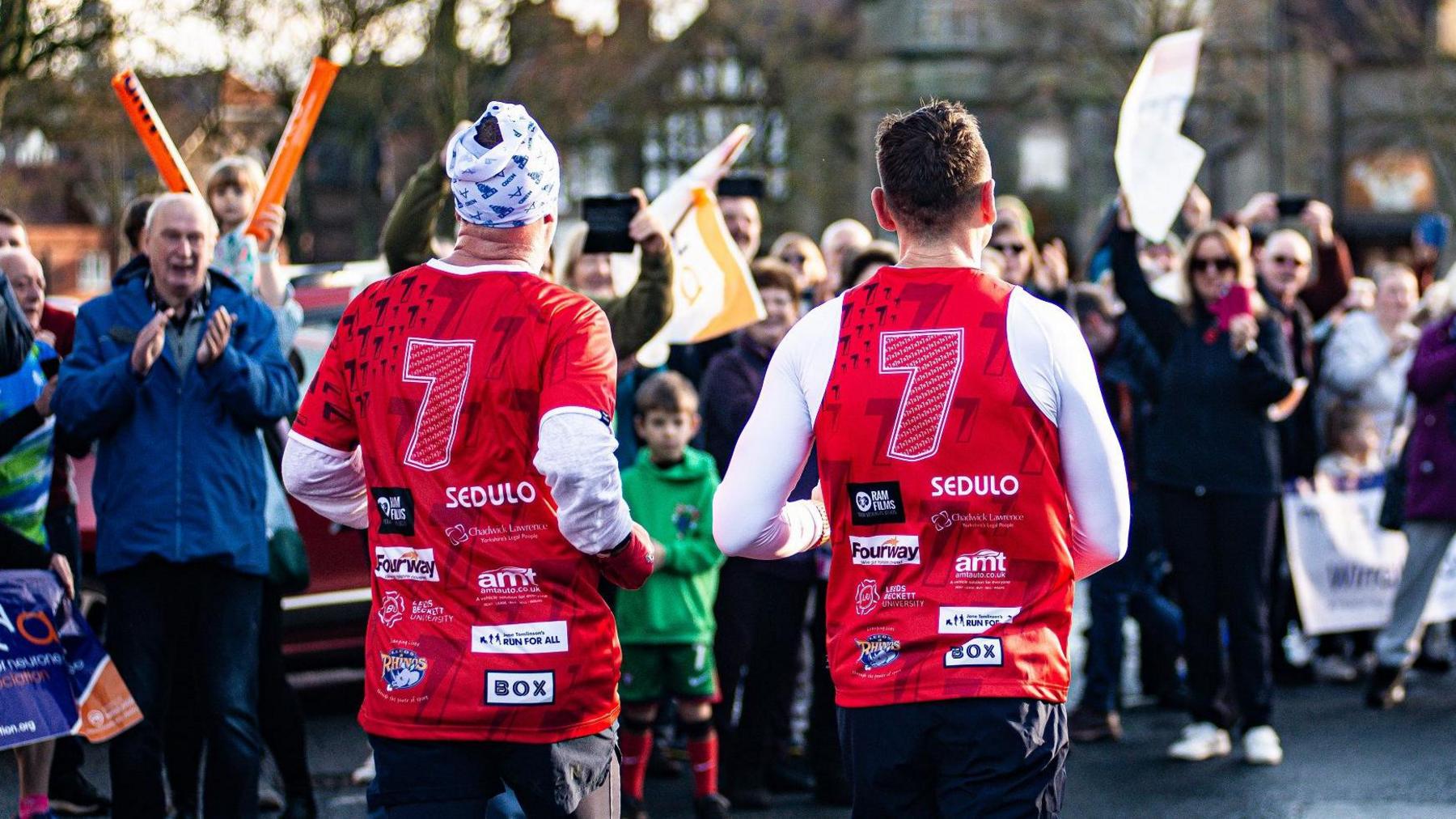 Sinfield and a support runner wearing tops with the number 7 while applauded by well-wishers lining their route