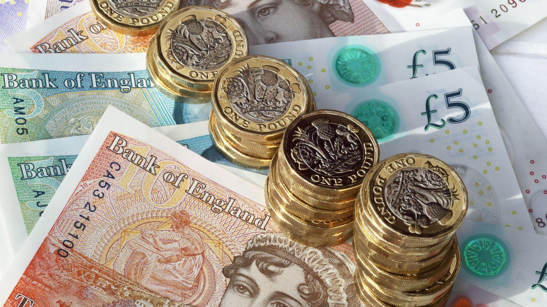 A graphic of stacks of pound coins on top of ten and five pound notes. 