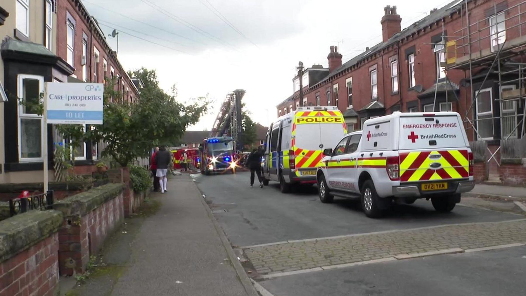 Emergency service vehicles parked on a residential terraced street in Leeds.