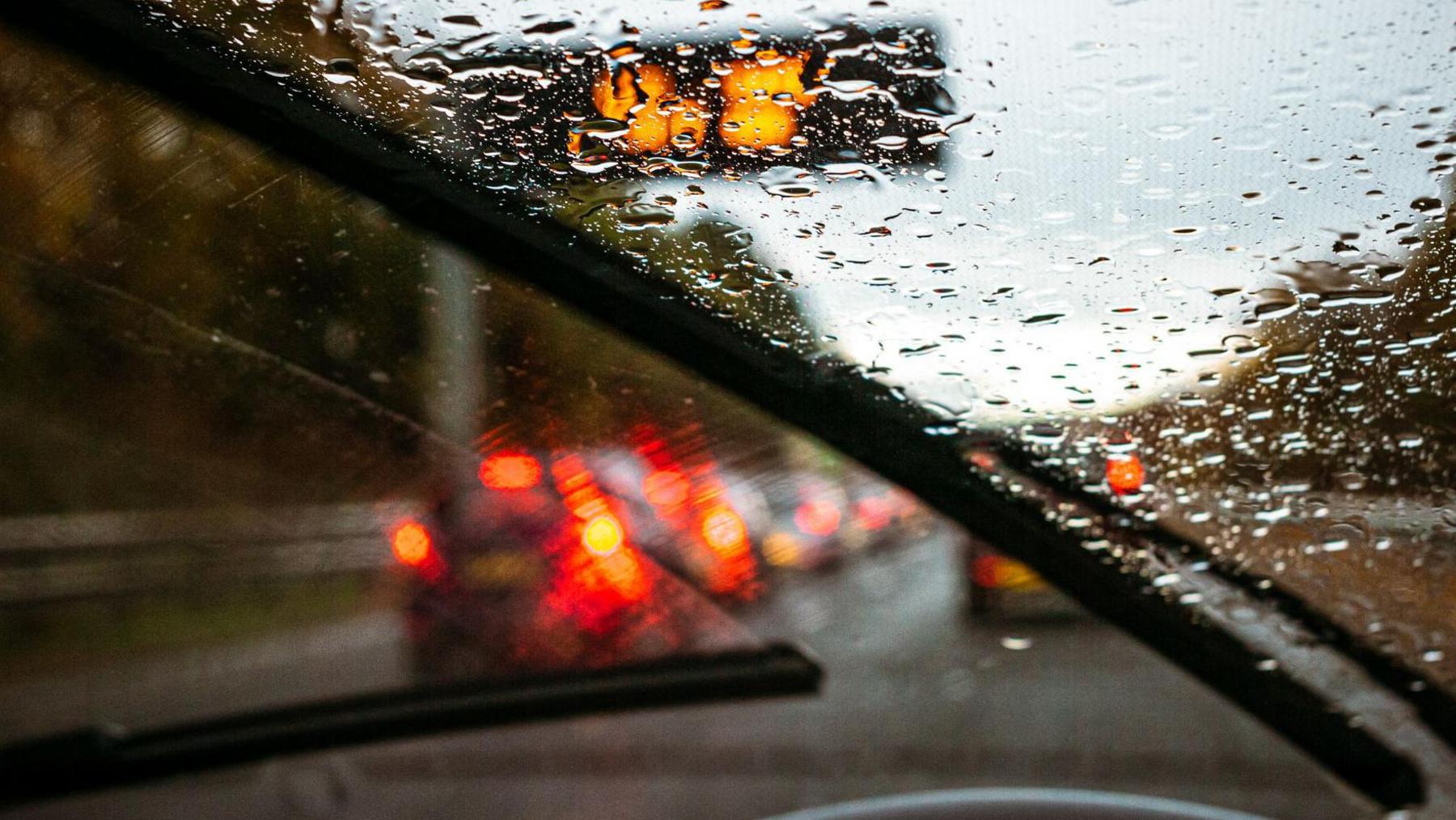 A stock image of a rainy windscreen of a car waiting in traffic on a motorway