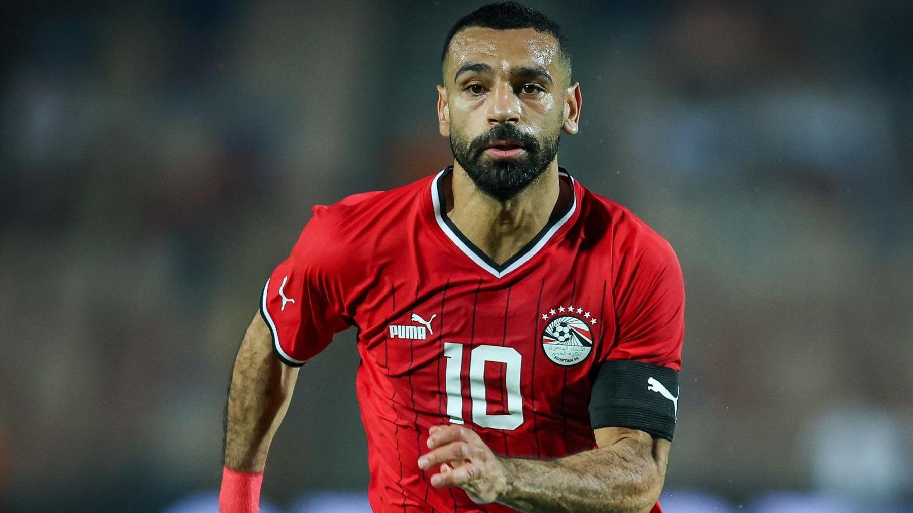 Mohamed Salah wears a red Egypt shirt and black captain's armband as he runs towards the camera during a football match