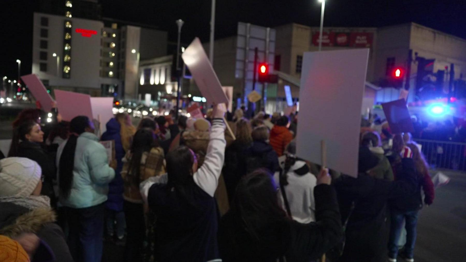 People in Plymouth city centre taking part in a Reclaim the Night march. Many of the people in the crowd which is lining the street in Plymouth are holding up placards.