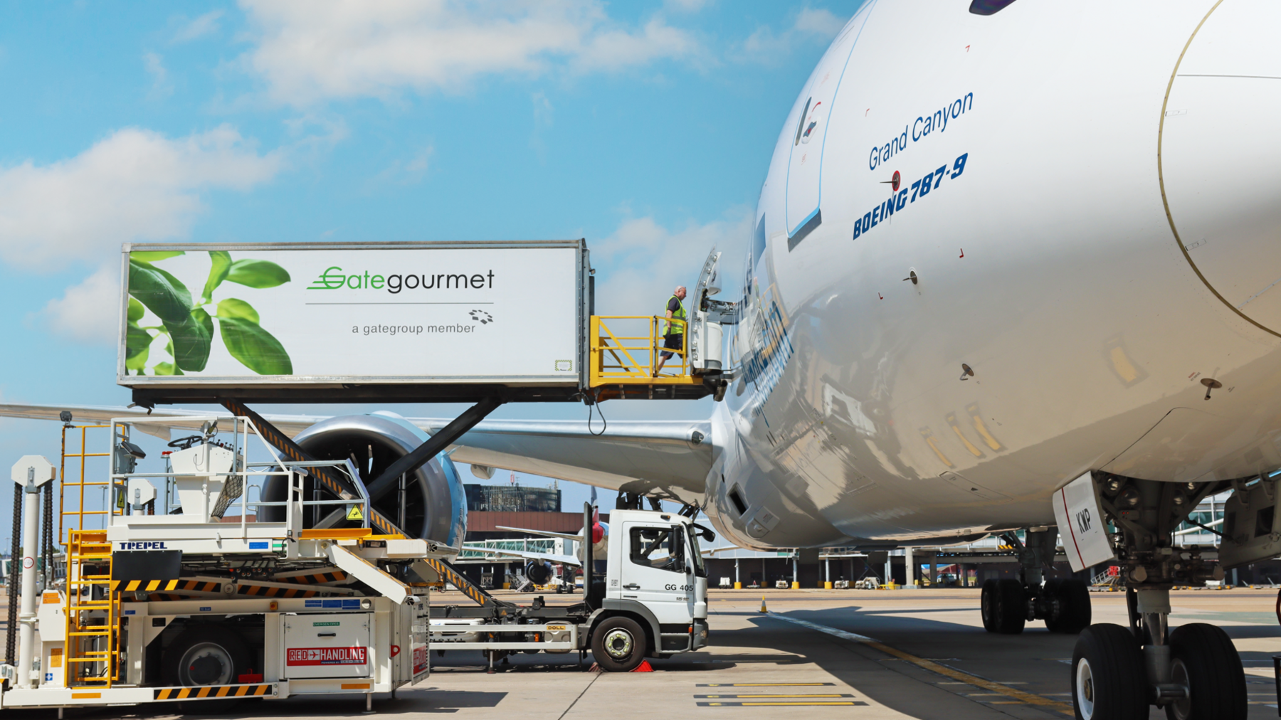 A white plan with a cargo import container next to it. There is a man in a high-visibility jacket and a vehicle next to the plane. 