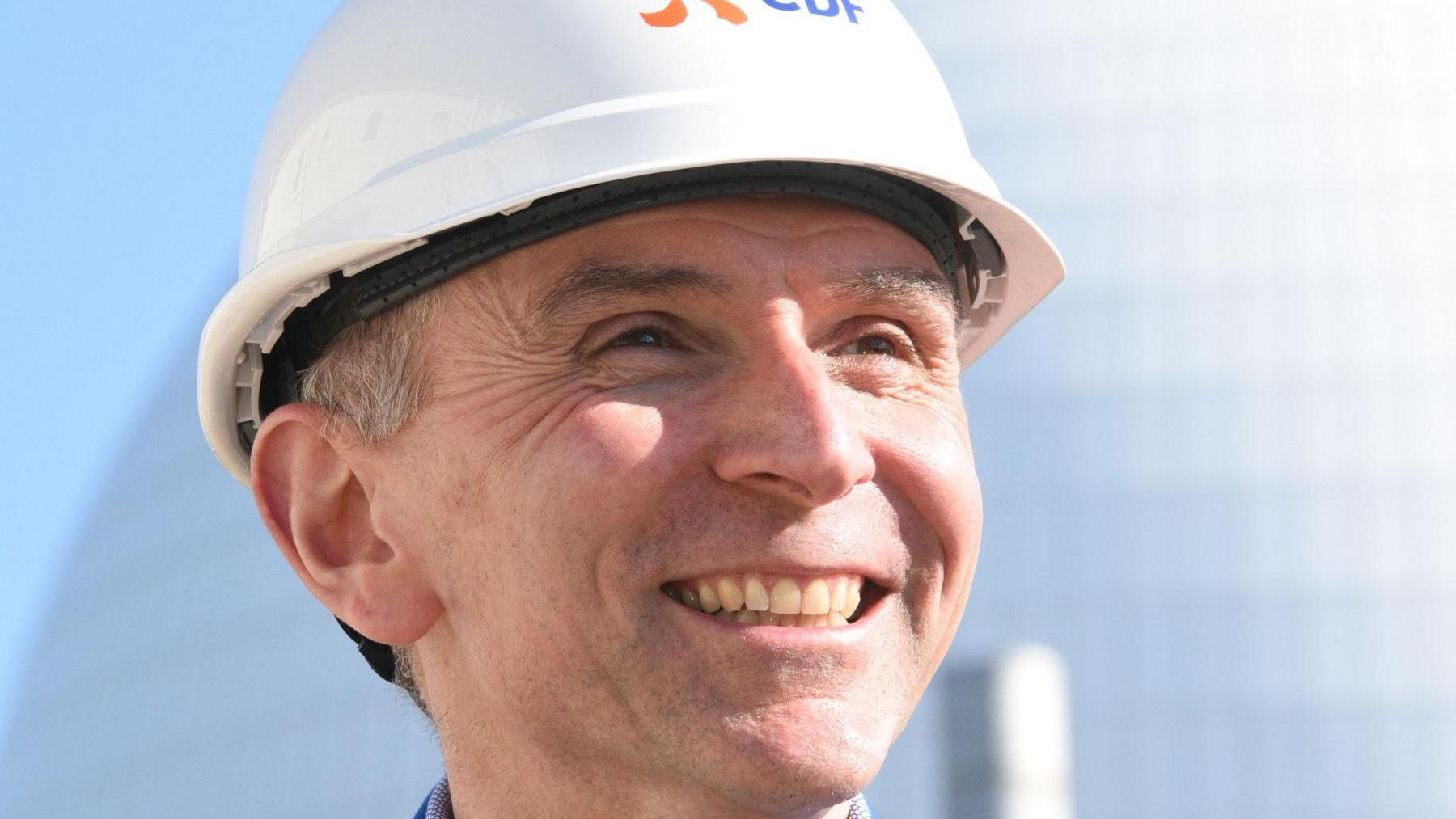 A general view of Sizewell B station director Robert Gunn. The close-up photo shows him looking past the camera and smiling. He is wearing a white EDF hard hat. 