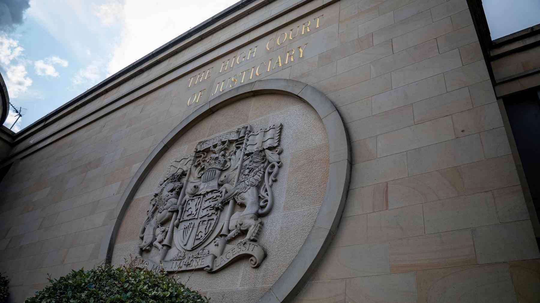 An exterior sandstone wall of the High Court in Glasgow with a crest.
