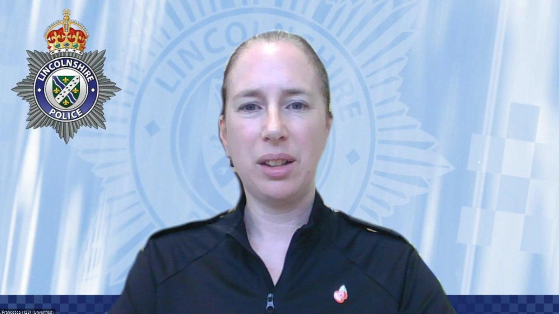 An image from a Zoom call showing Supt Fran Harrod in front of a virtual light-blue backdrop featuring a Lincolnshire Police logo. Supt Harrod has blonde hair, tied back, and wears a black zip-neck top with a Poppy badge.