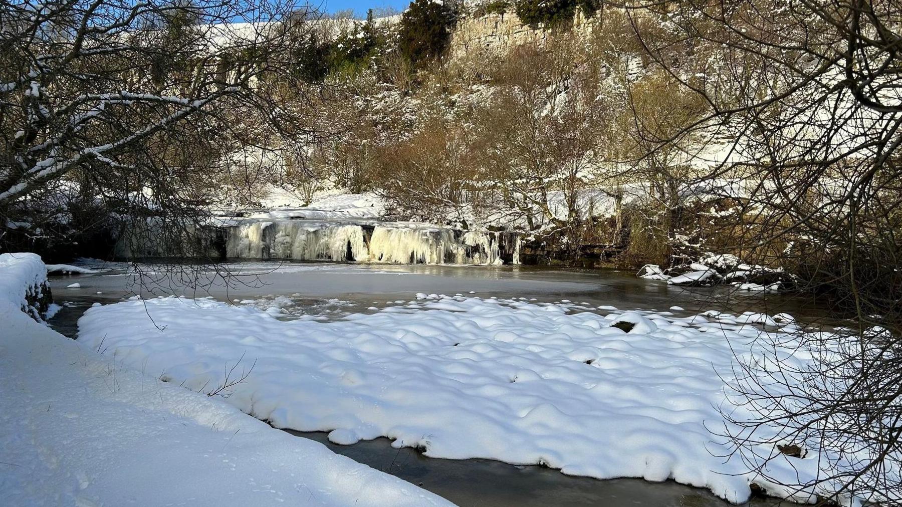 Wainwath Falls: a small frozen waterfall in the Yorkshire Dales with trees behind it.