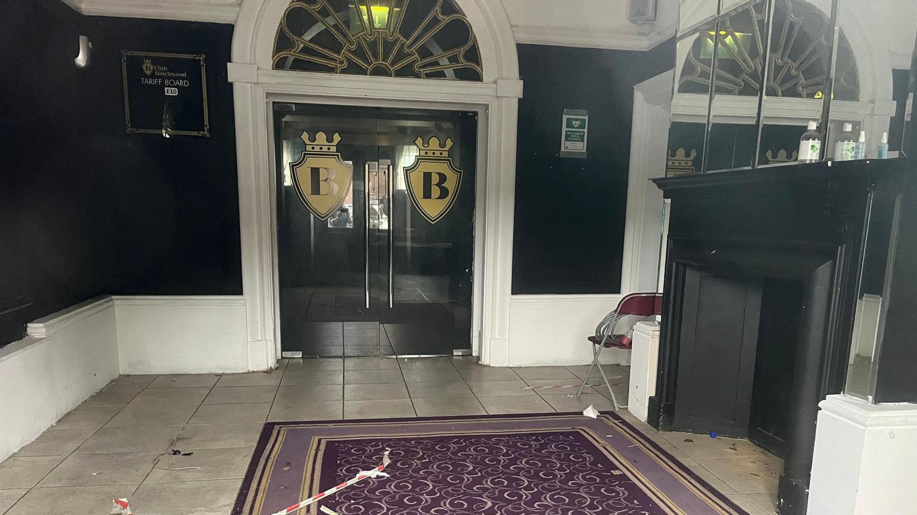 Entrance lobby to a nightclub in a Victorian building, with a purple rug on a tiled floor, black walls and the letters E and B embossed on doors