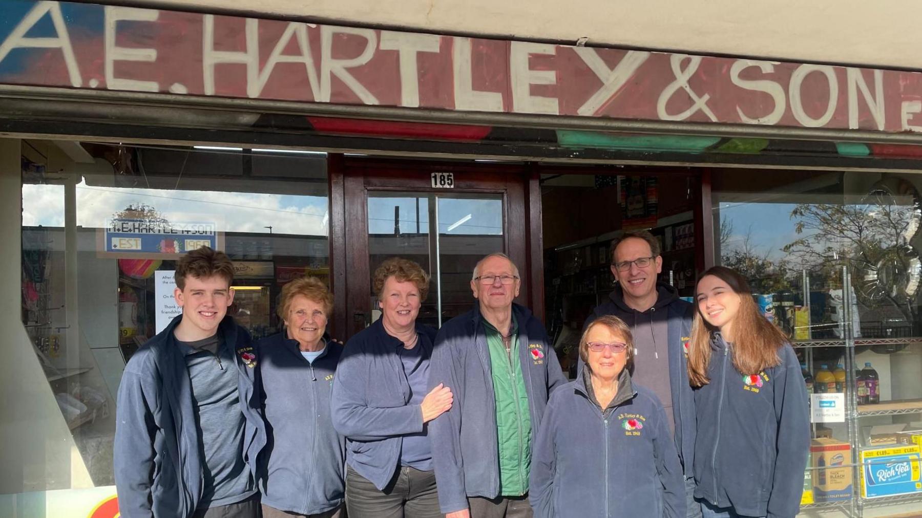 A group shot of people of all ages in matching navy fleeces outside a shop.