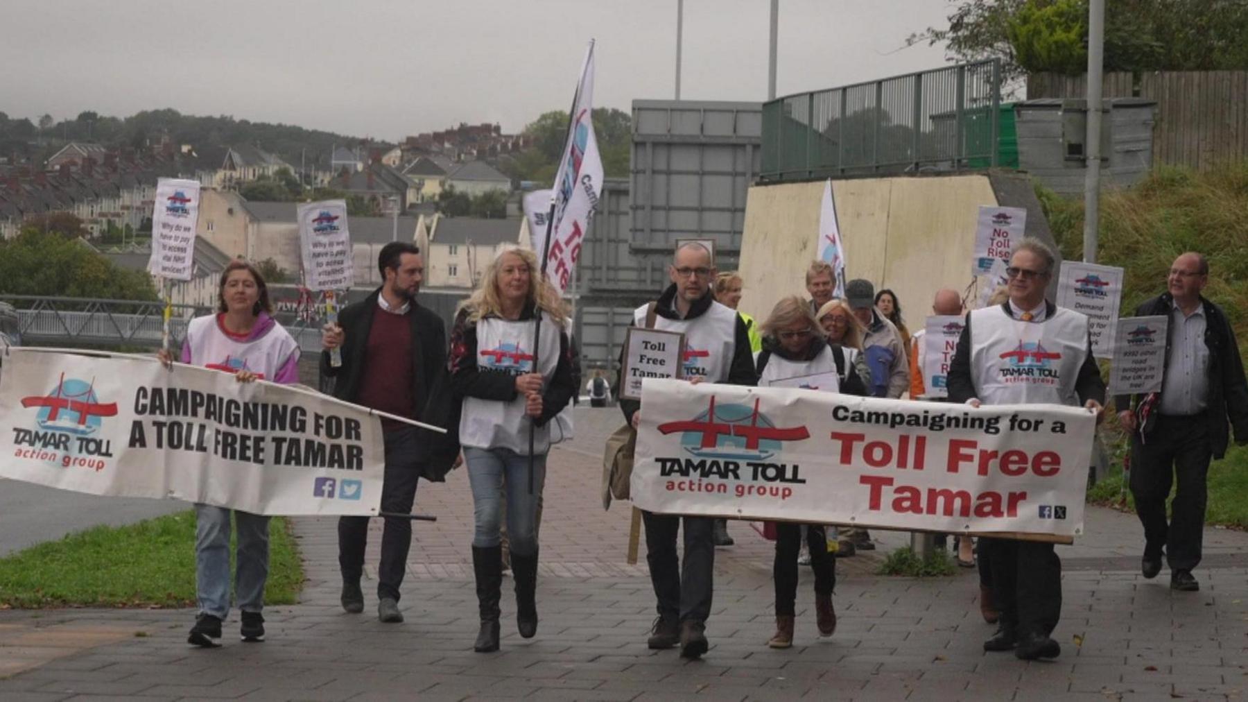 A group of campaigners from the Tamar Toll Action Group walking up a street with banners calling for the crossings to be free.