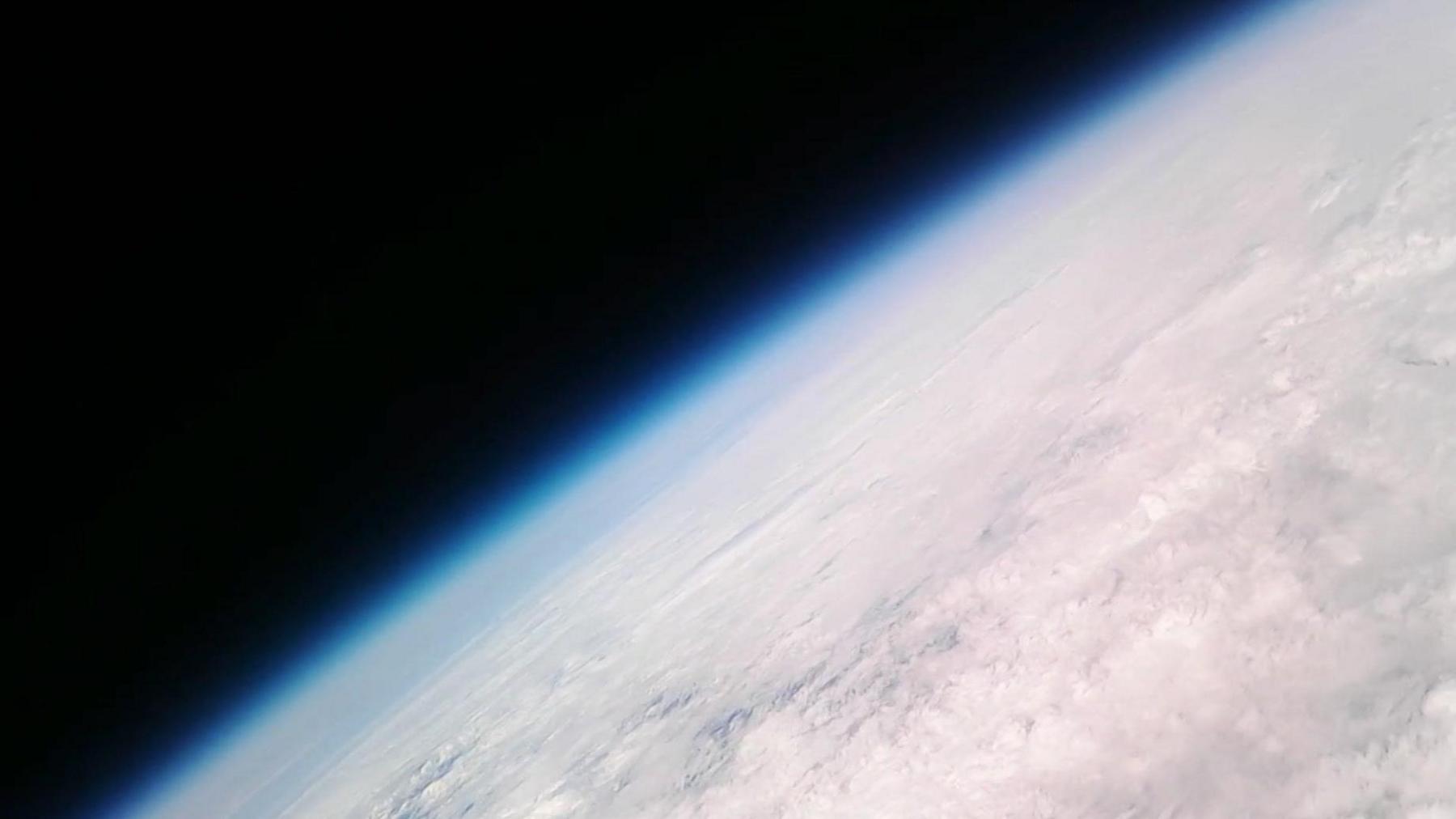 An image from a camera at high altitude of the earth and space beyond it. There is a distinct haze of atmosphere visible. 