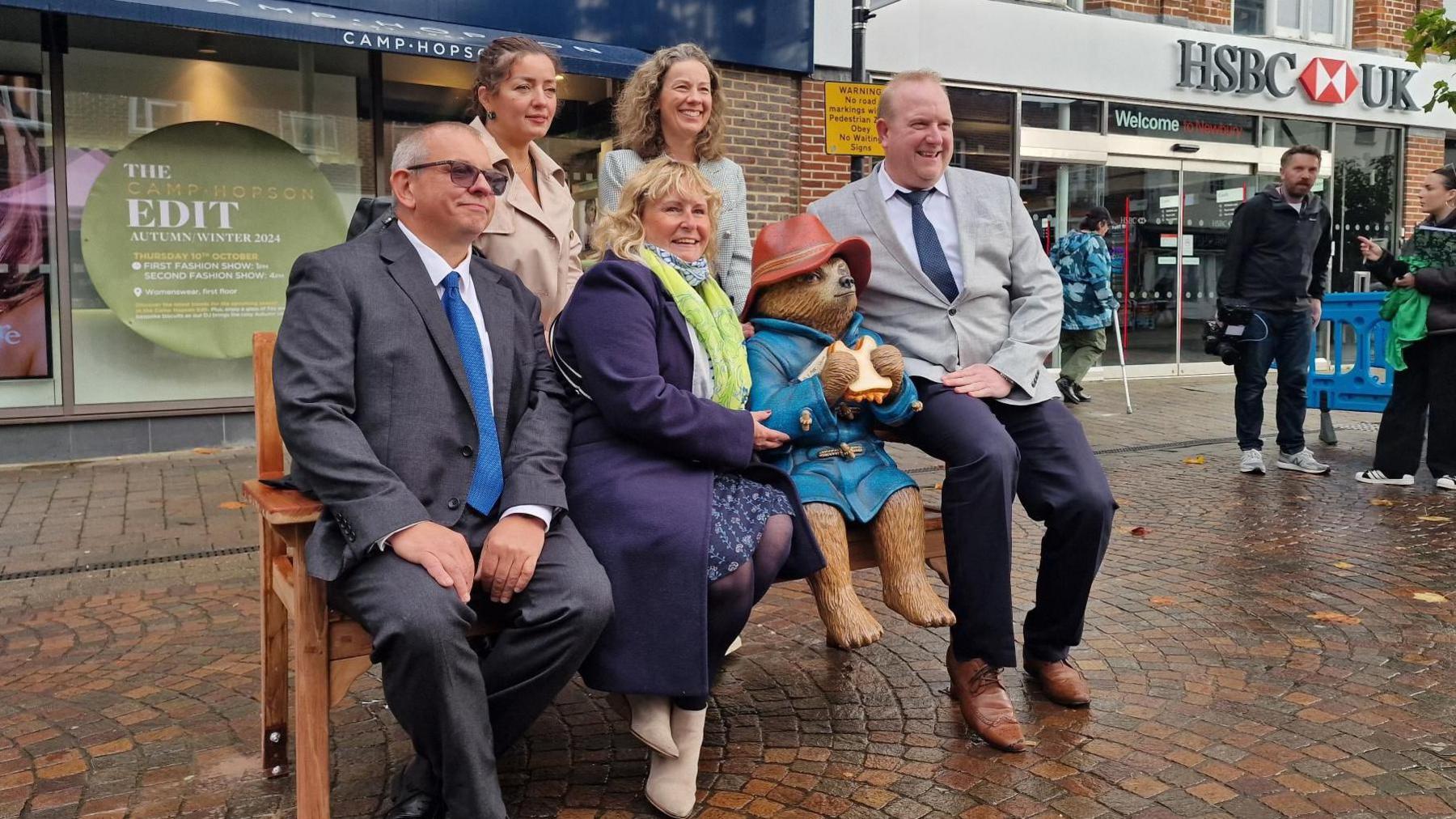 Two men and three women smiling with the statue of Paddington.