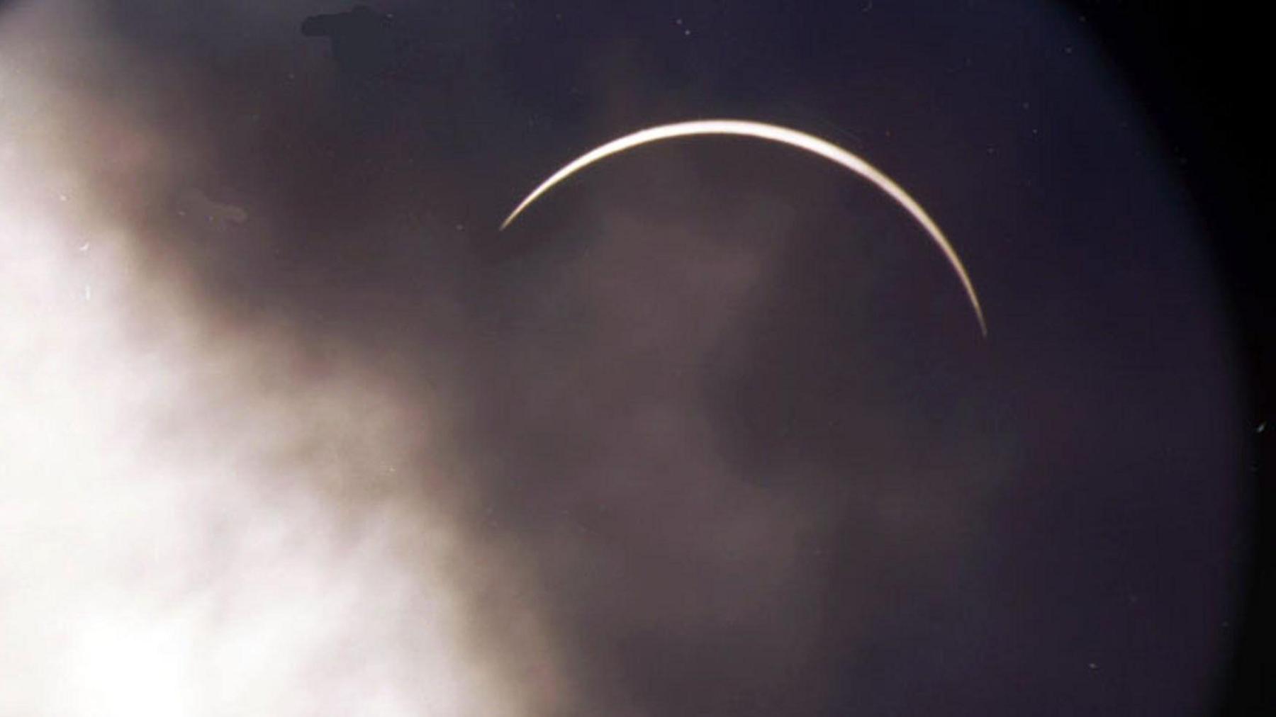 The moon is covering the sun, leaving a fingernail of light. The cloud over the moon is dark and there is lighter cloud to the left.