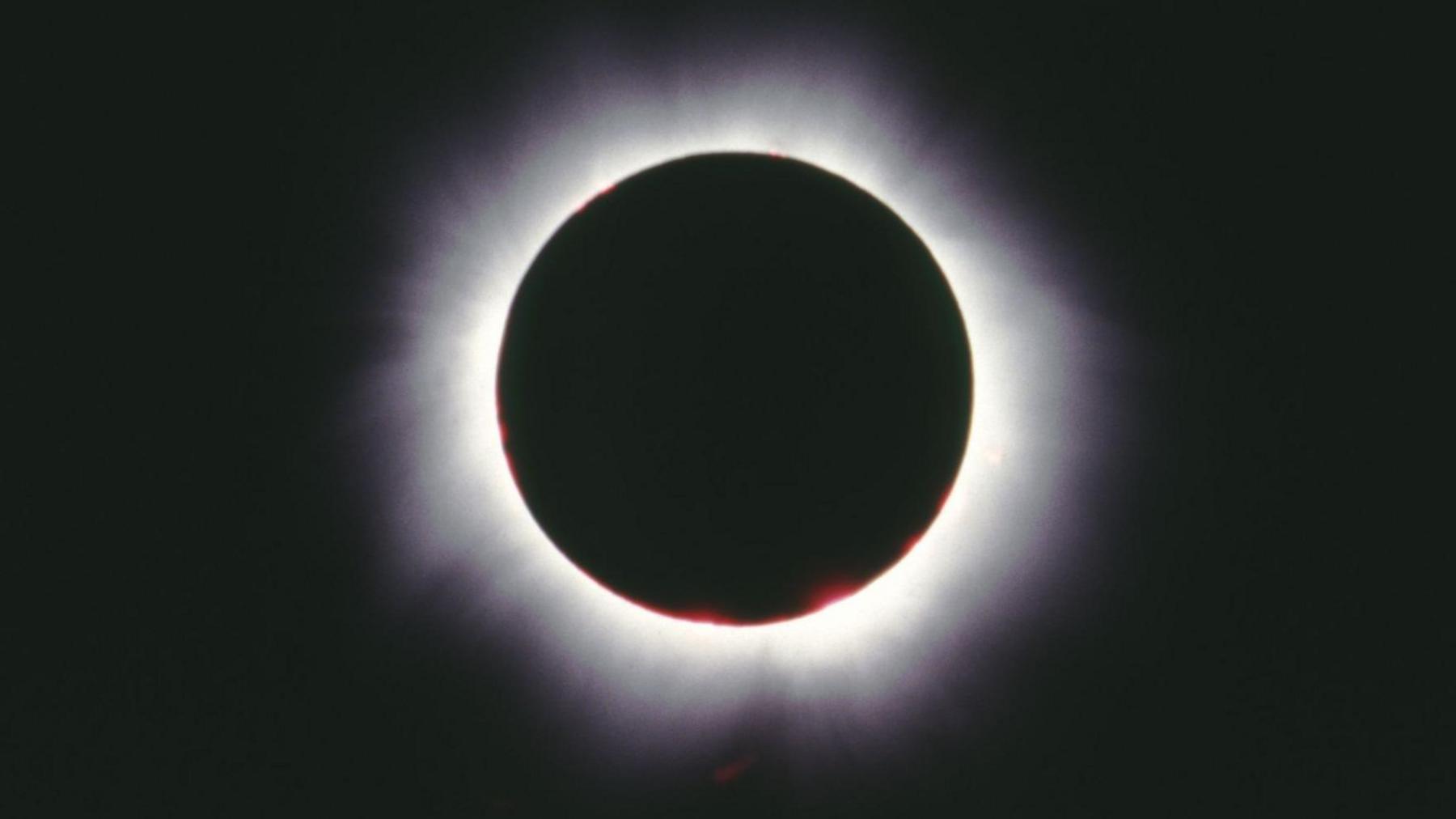 A total solar eclipse - a black circle with a glowing white outline, in a dark sky. 