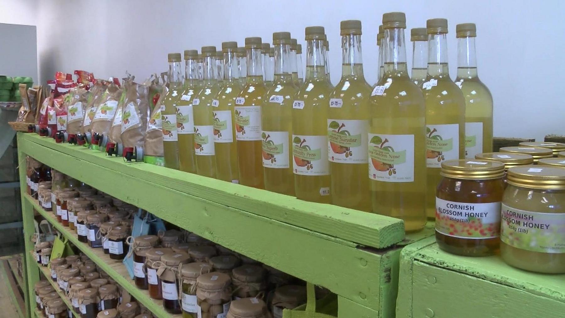 Jars of jam and honey and bottles of apple juice on green shelves