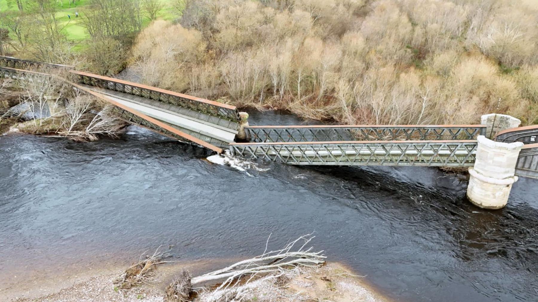 A collapsed iron girder bridge with a section between two stone piers breaking apart and falling into the water
