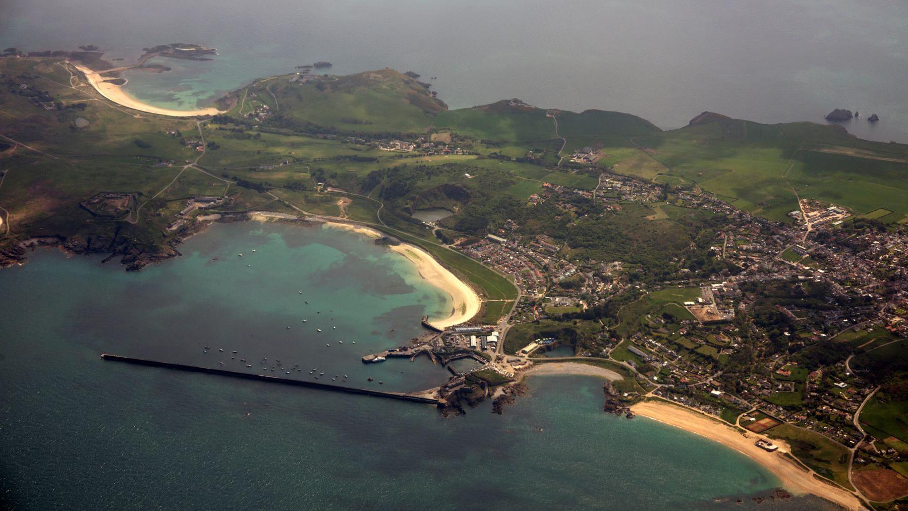 A small island with sandy beaches, fields and a small town from above.