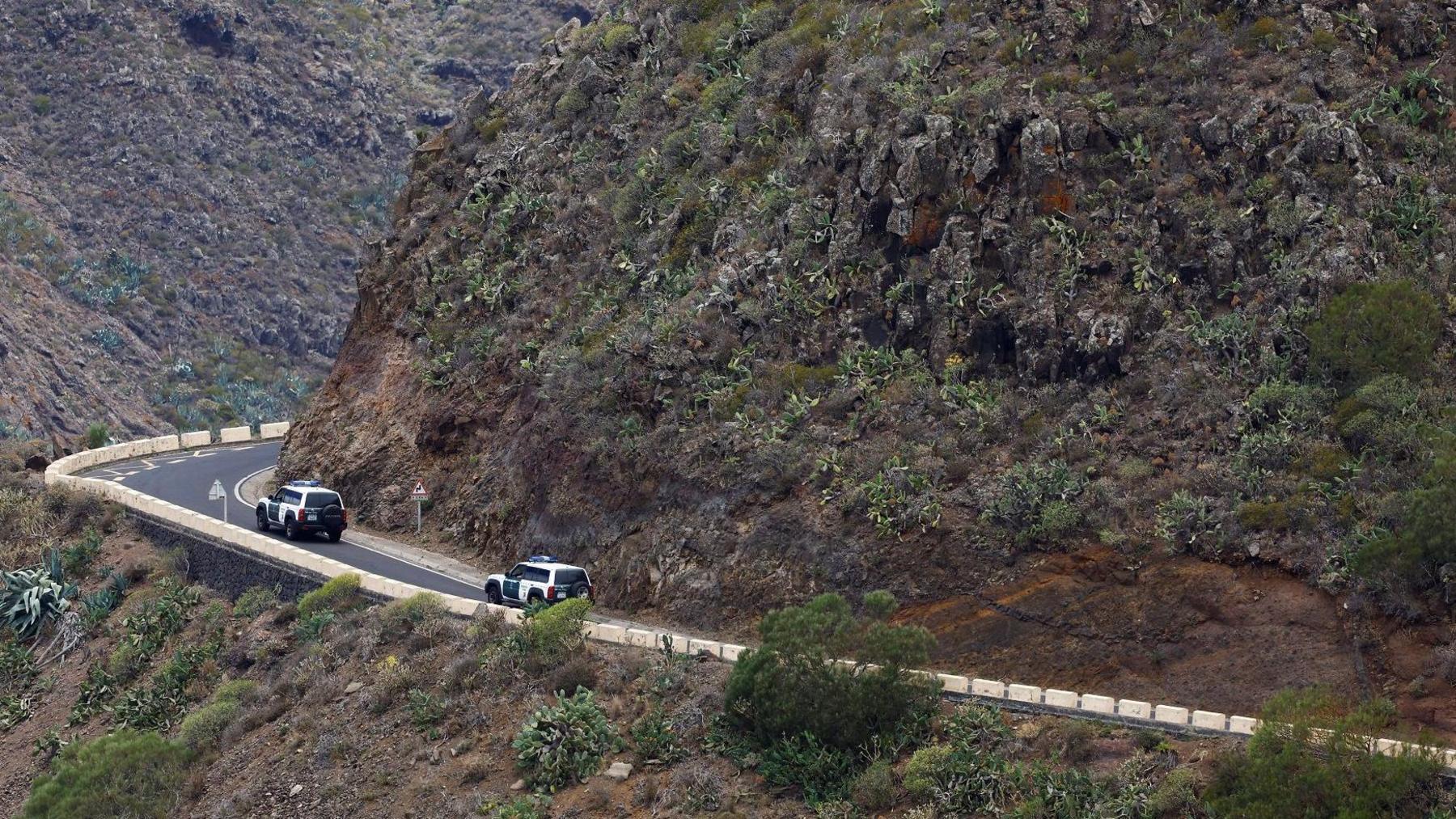 Two 4x4 vehicles belonding to Spanish authorities drive on road winding around edge ot rocky mountain covered in shrubs in the national park