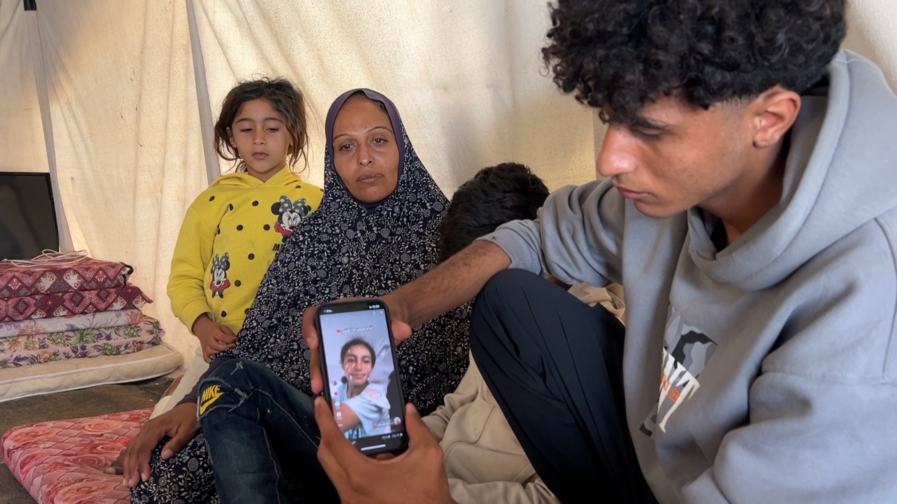 Family members in a tent show pictures of Aya on a mobile phone 