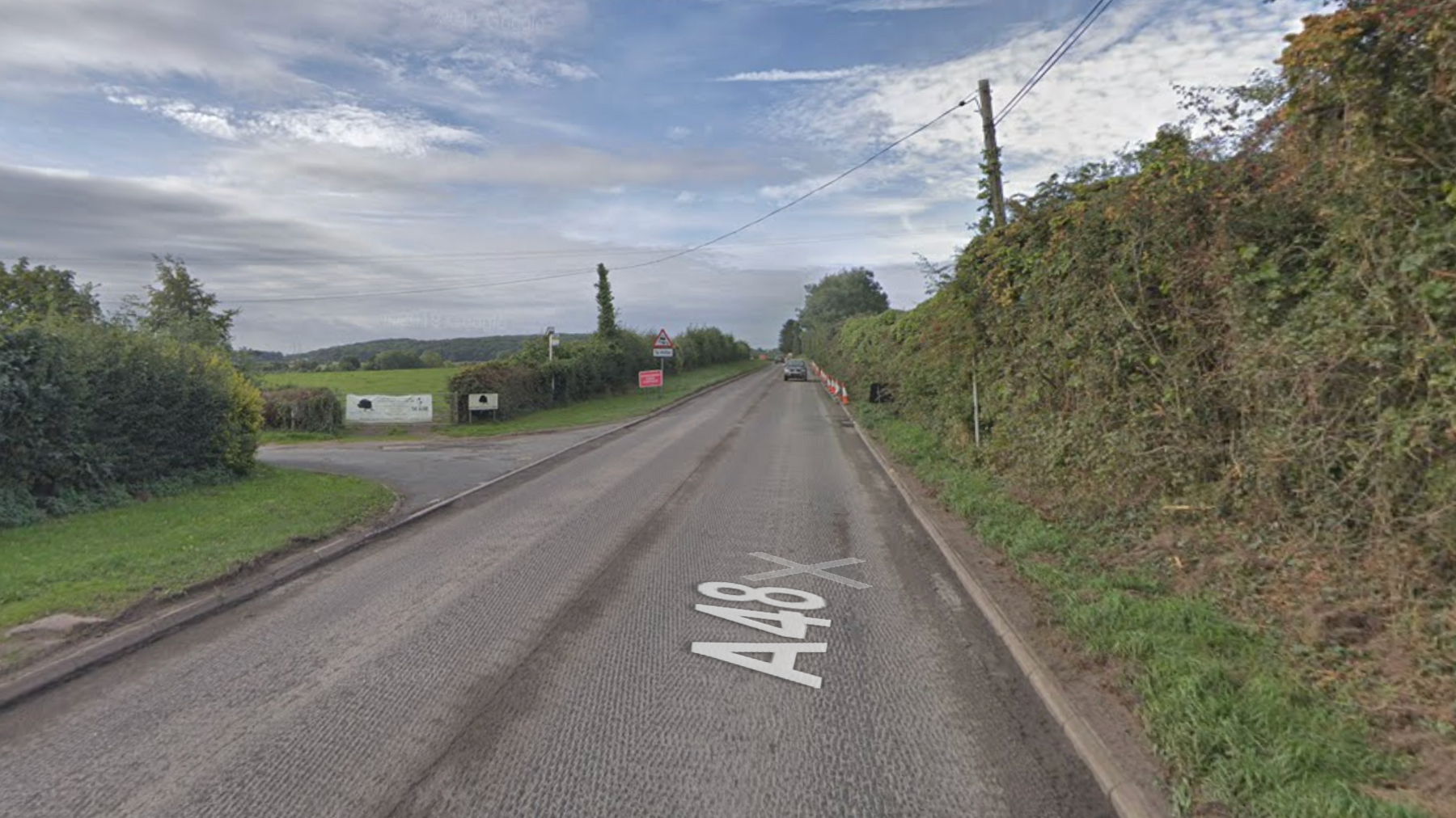 Google maps street view of the Severndale Farm junction in Tidenham. The road has no markings. The junction to the farm is on the left and there is a hedge the other side of the road.