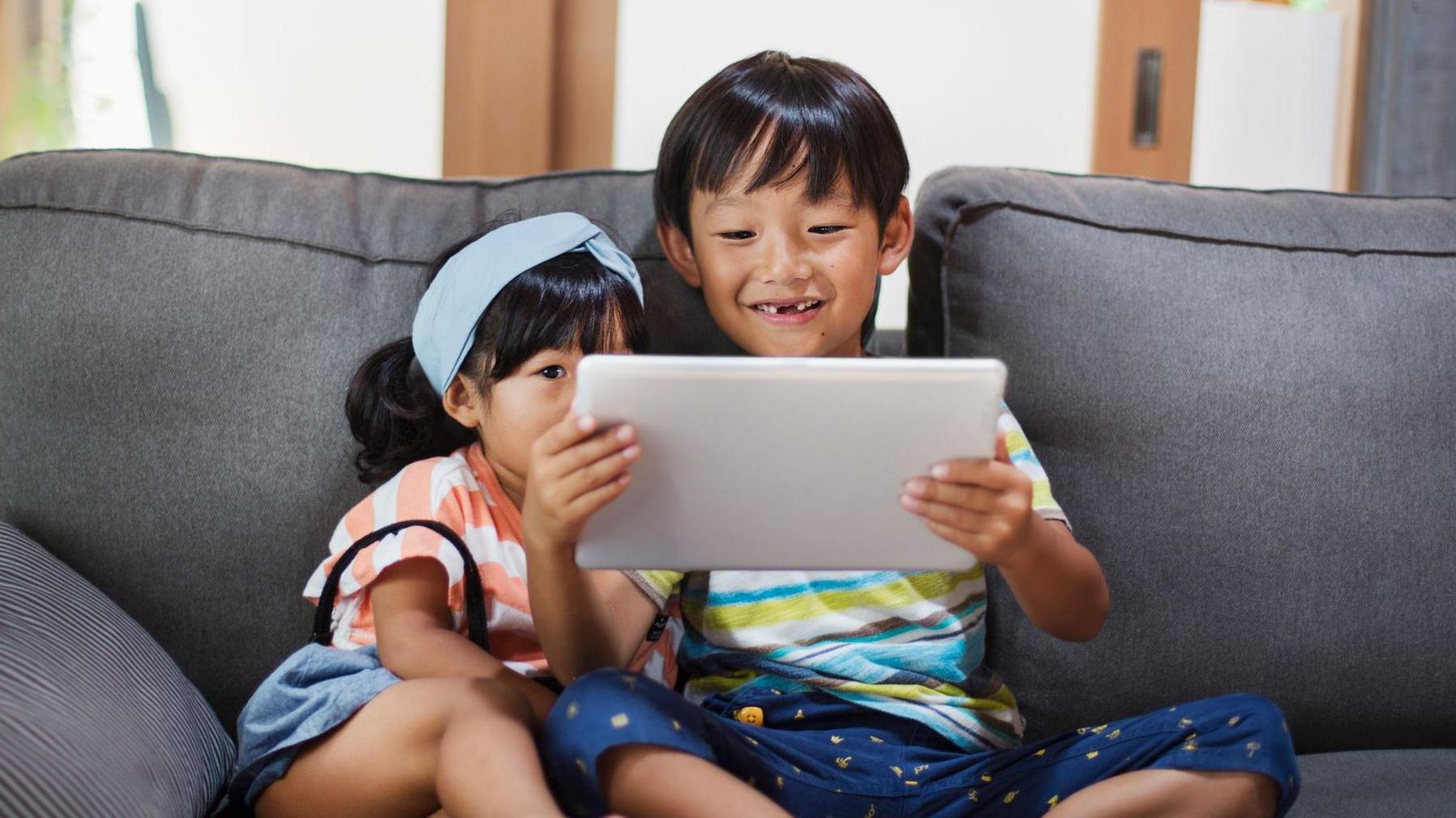 children looking at tablet while sat on sofa.