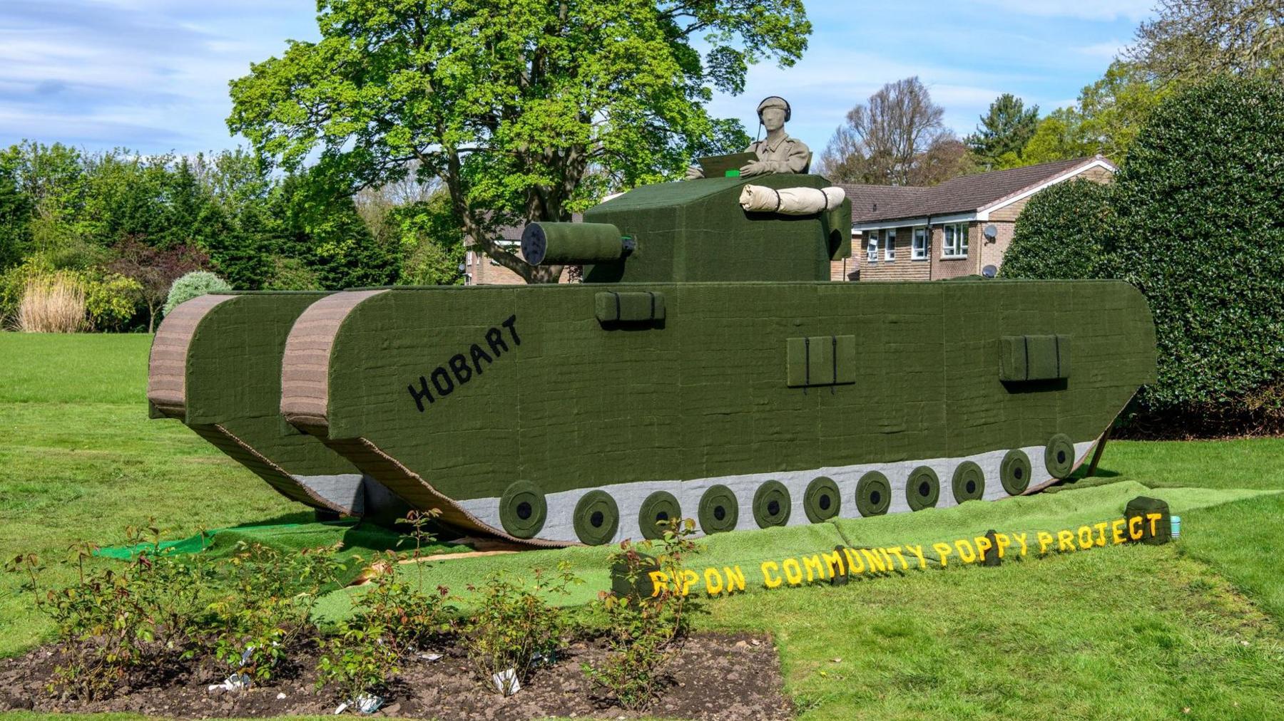 Life-size knitted tank, mainly green in colour, including a gun turret