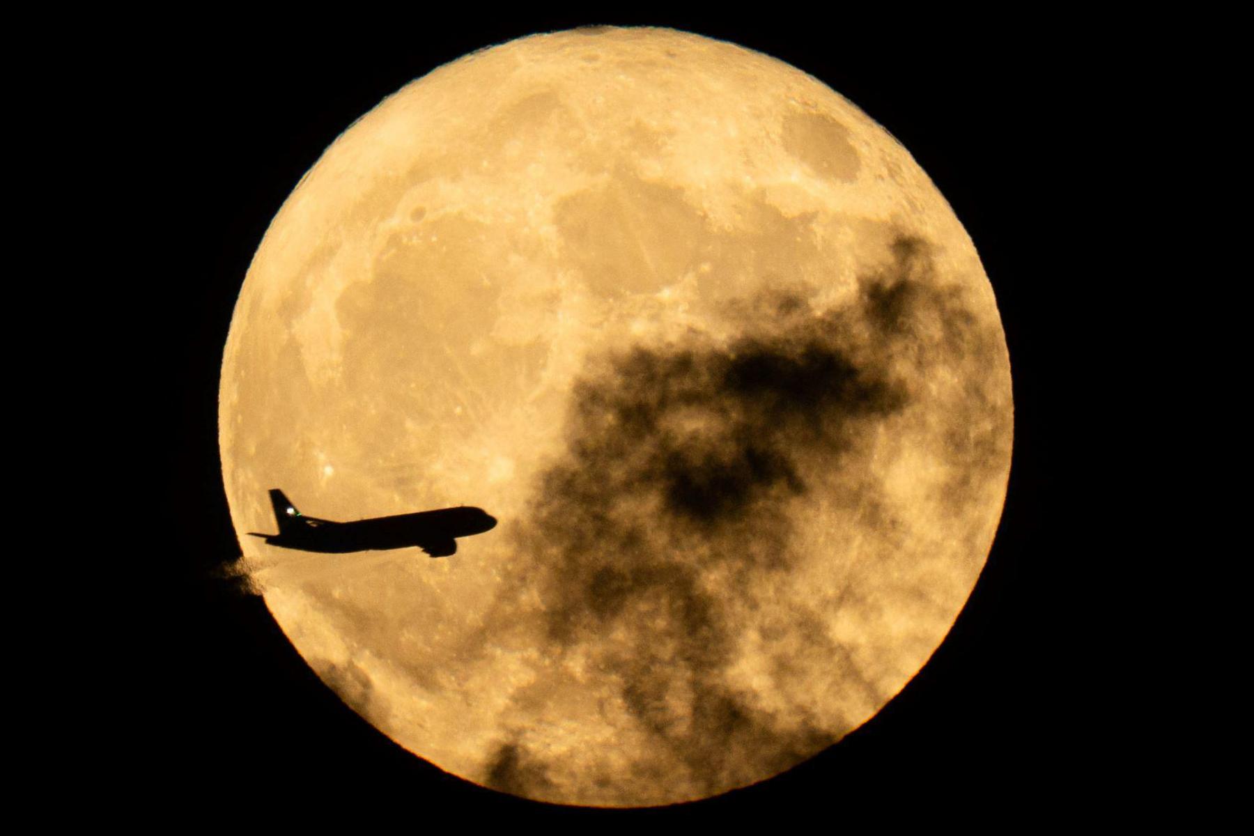 A plane flies in front of the full Moon
