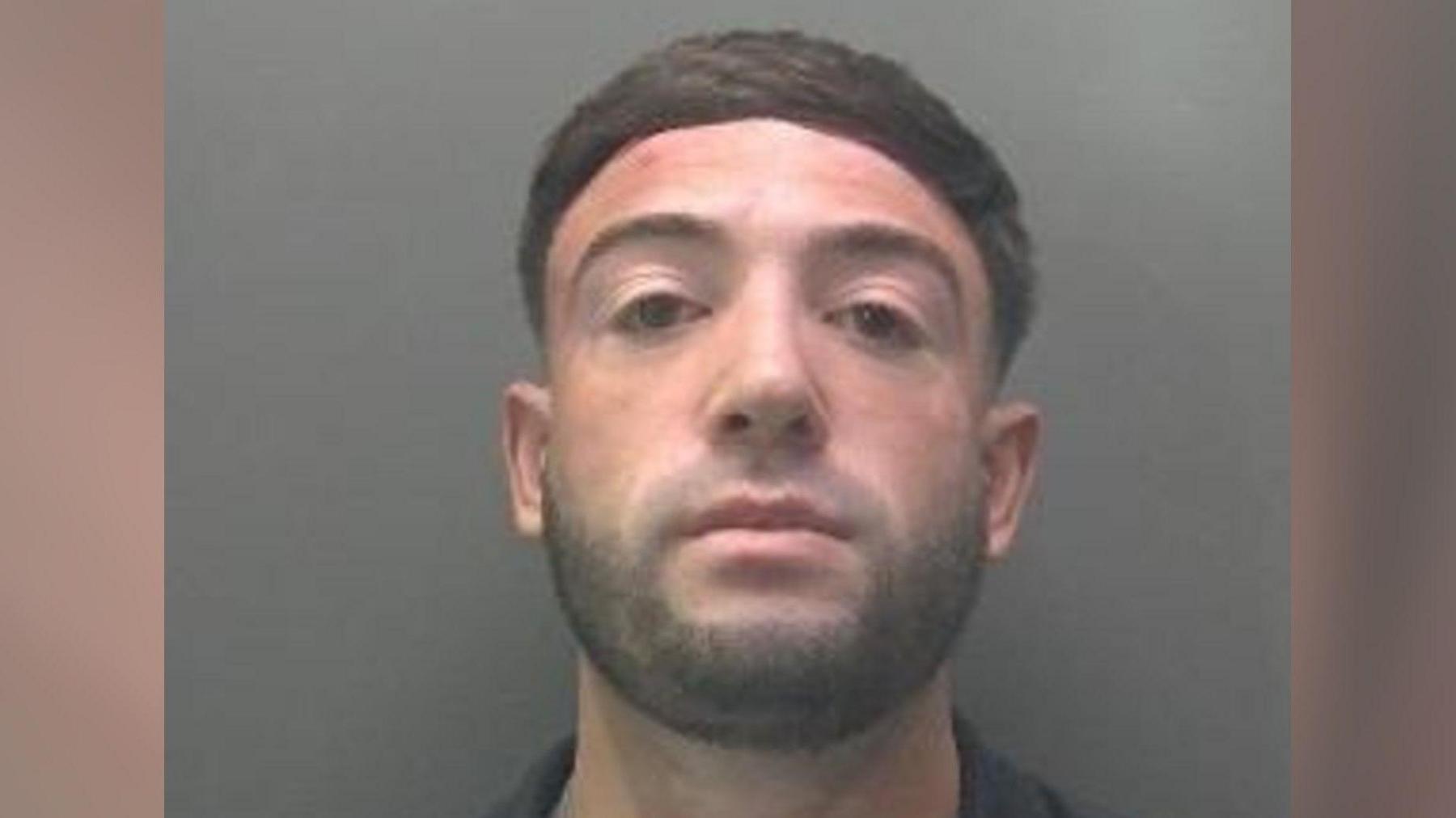 Custody image of Dominic Bevilacqua - he is looking into the camera with his chin raised. he has black hair and a short stubble beard