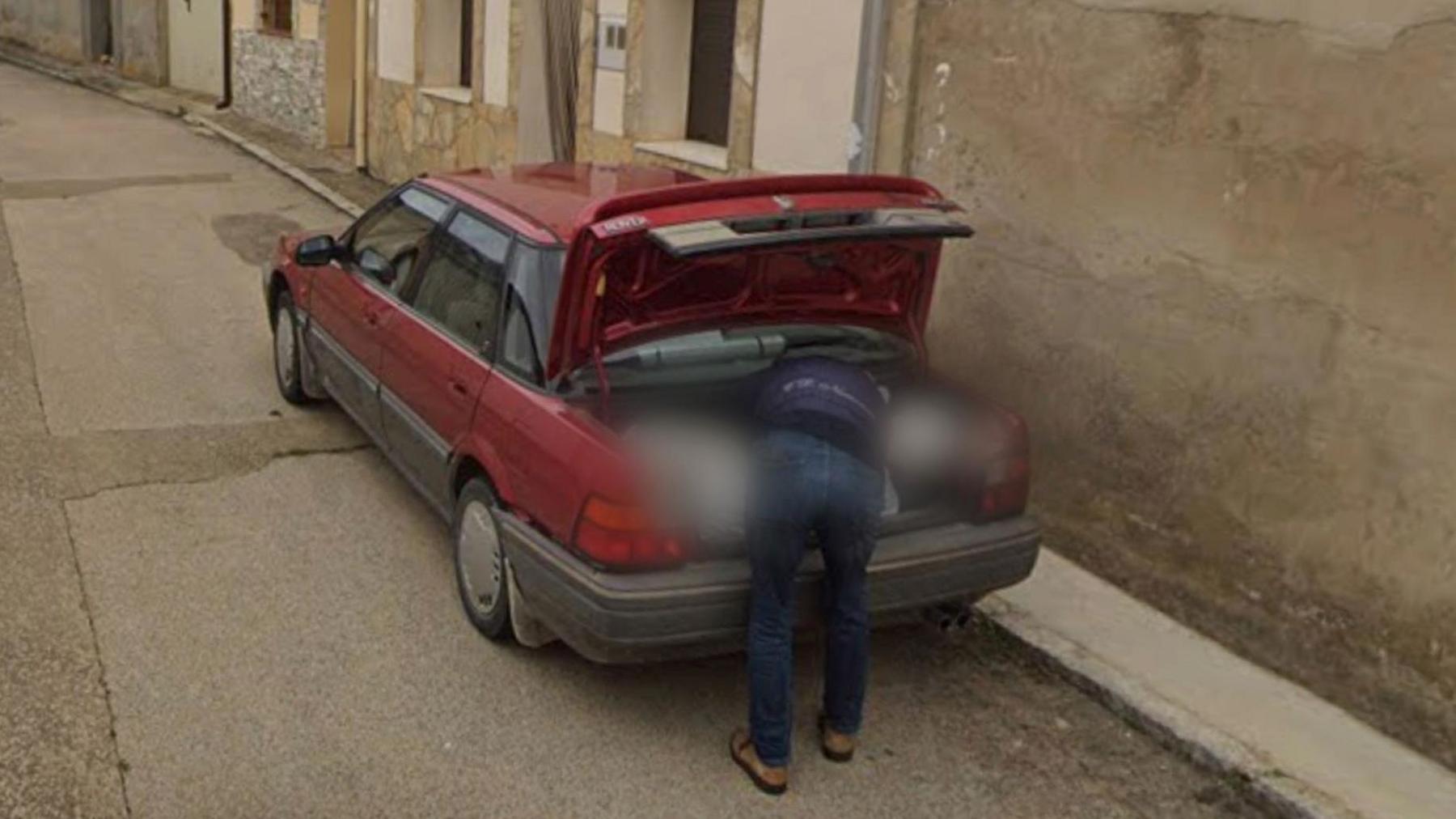 Google Streetview image of man putting plastic bag in boot of car parked on town street