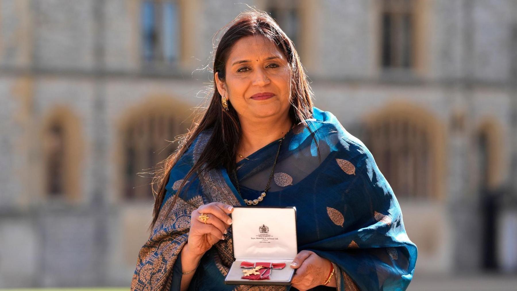 a woman proudly holds her OBE medal