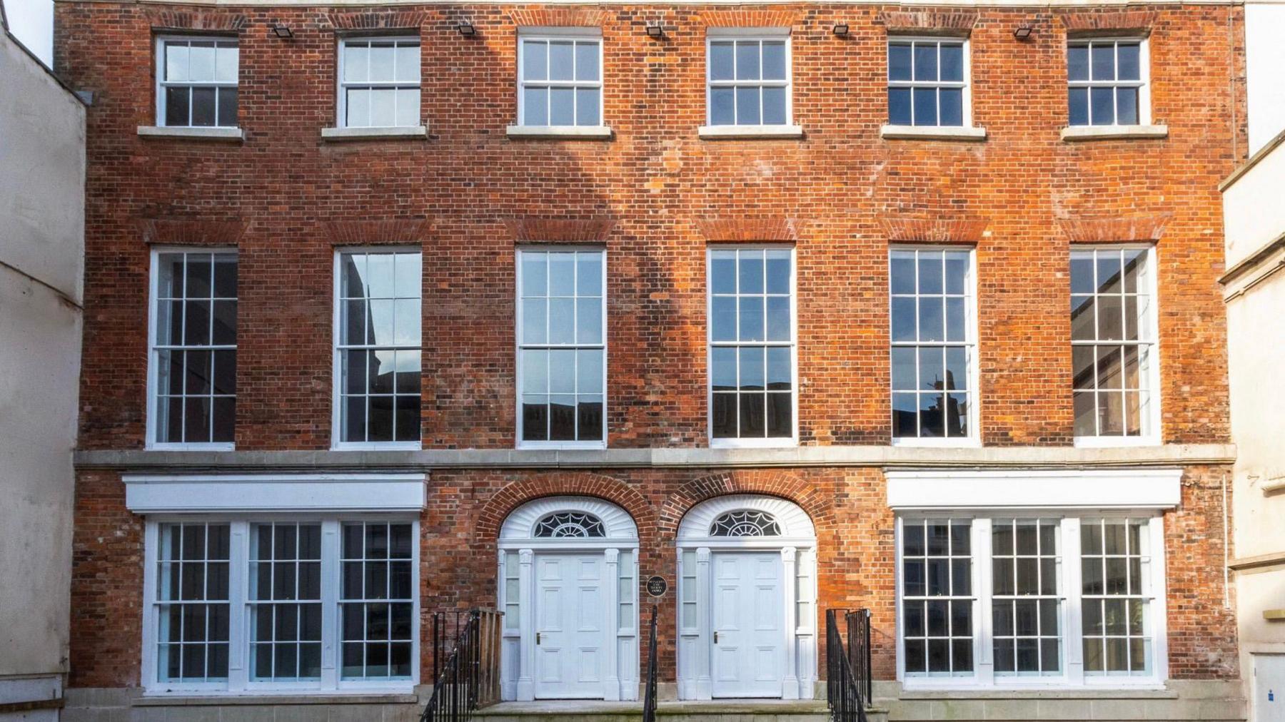 The front of the Rectory building. Two brick Georgian town houses knocked into one with large sash windows and a flight of steps going up to the two front doors which are side by side.