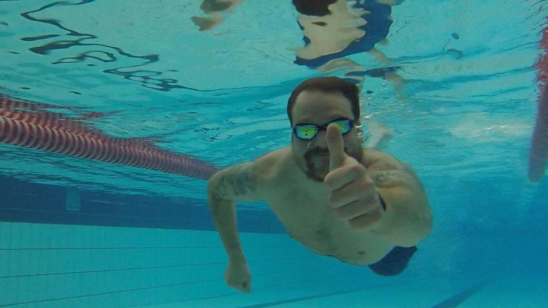 Jordan is swimming under water with his reflective goggles, and gives a thumbs up.