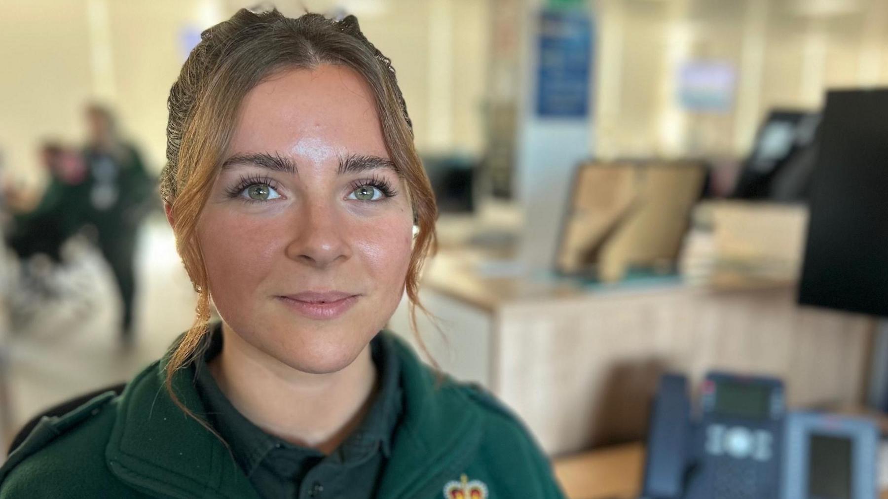 Hannah Dickson is pictured wearing her dark green ambulance service uniform. She has long brown hair tied back from her face. 