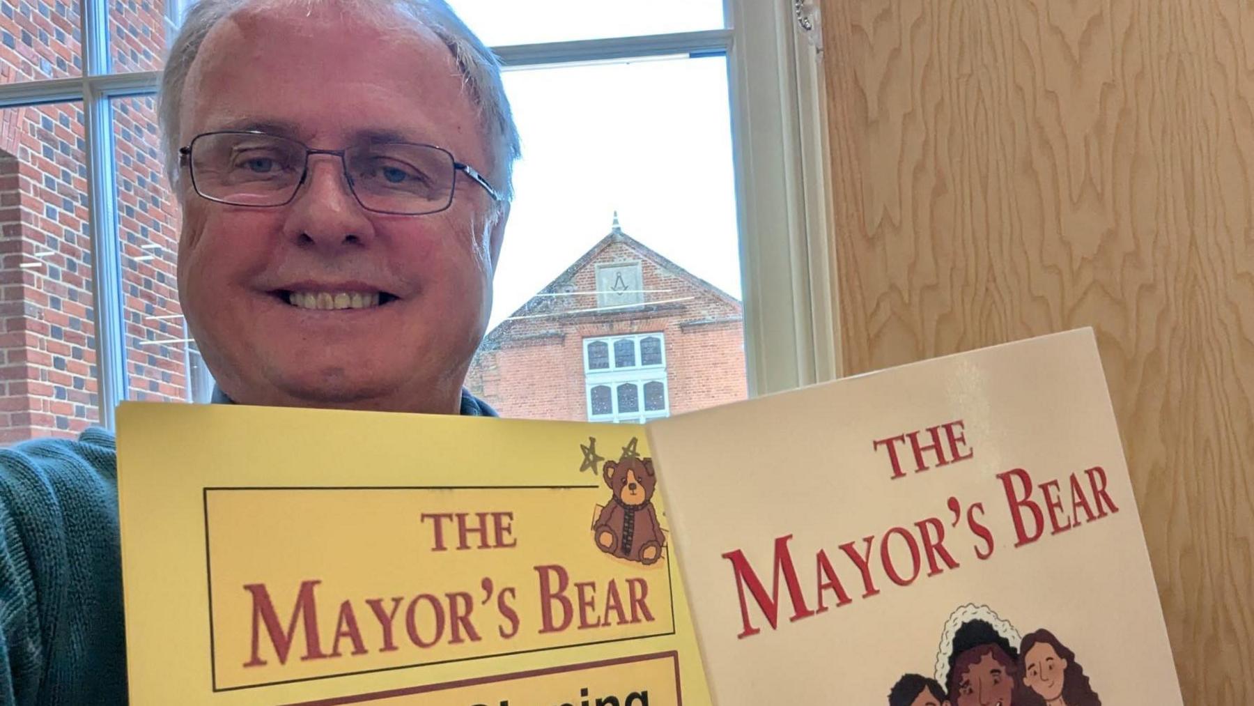 Jon Harvey taking a selfie with his book and a sign inviting people to get their own books signed. He is smiling and wearing glasses.