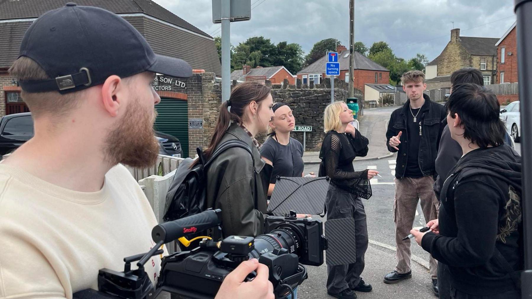 Young actors are stood on a street corner in Sheffield, with Jordan-Kane Lewis holding a camera in their direction.