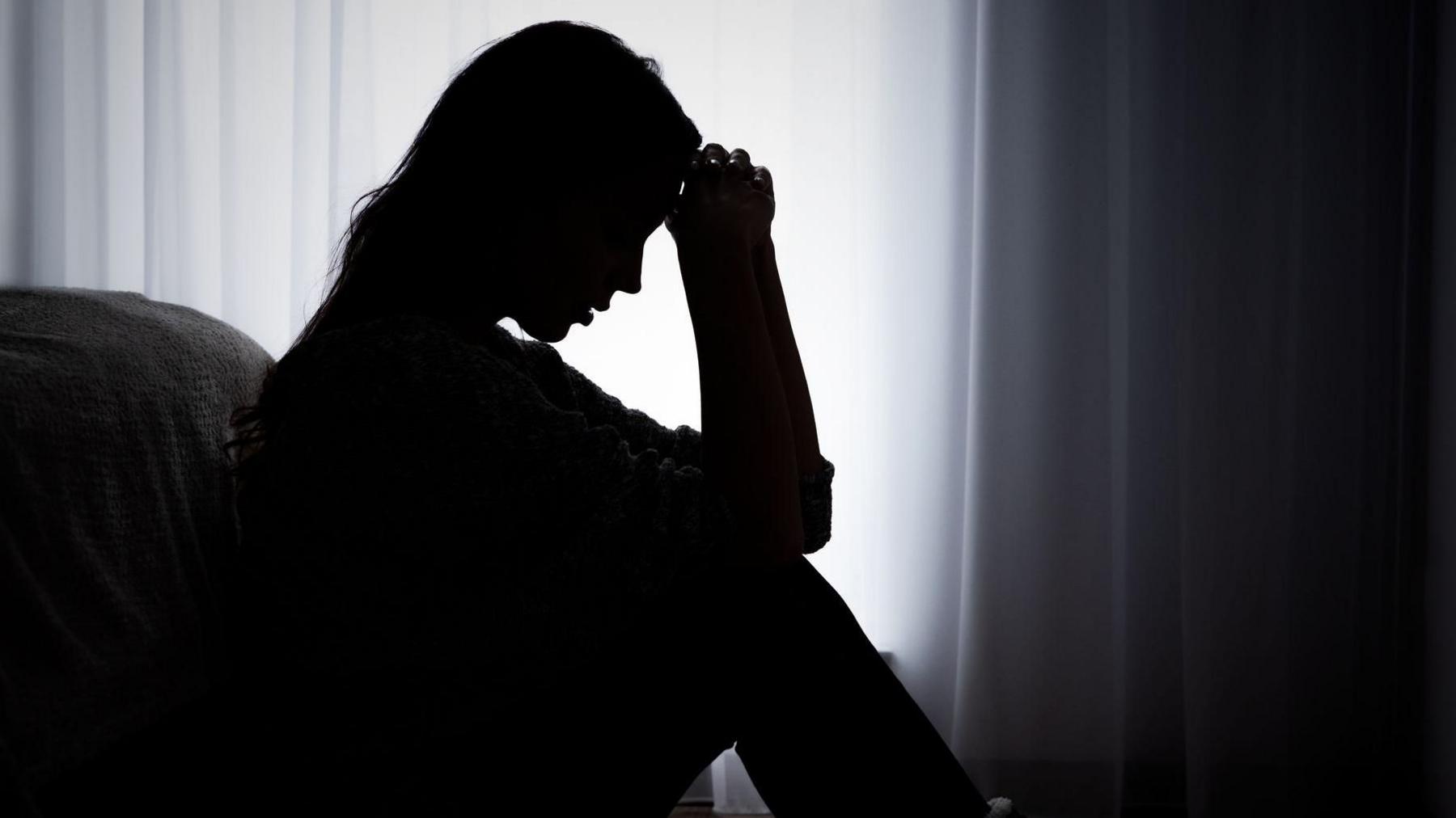 Silhouette of an anonymous woman sat looking distressed