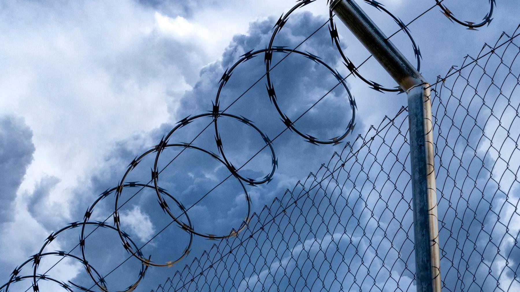 Close-up of metal fence with barbed wire over a stormy blue sky