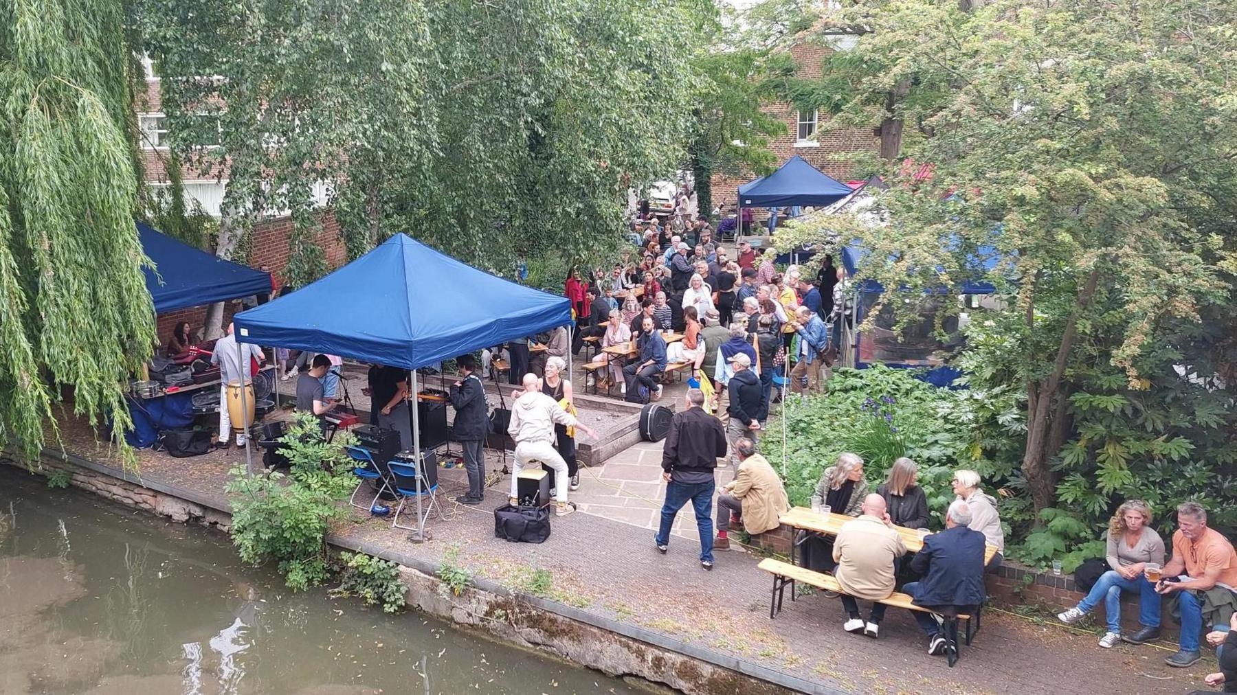 A shot from Mount Place bridge of a crowd of people at Mount Place during Jericho's Lazy Sunday in the summer. Some are buying food and drinks while others are watching a band perform. It's overcast.