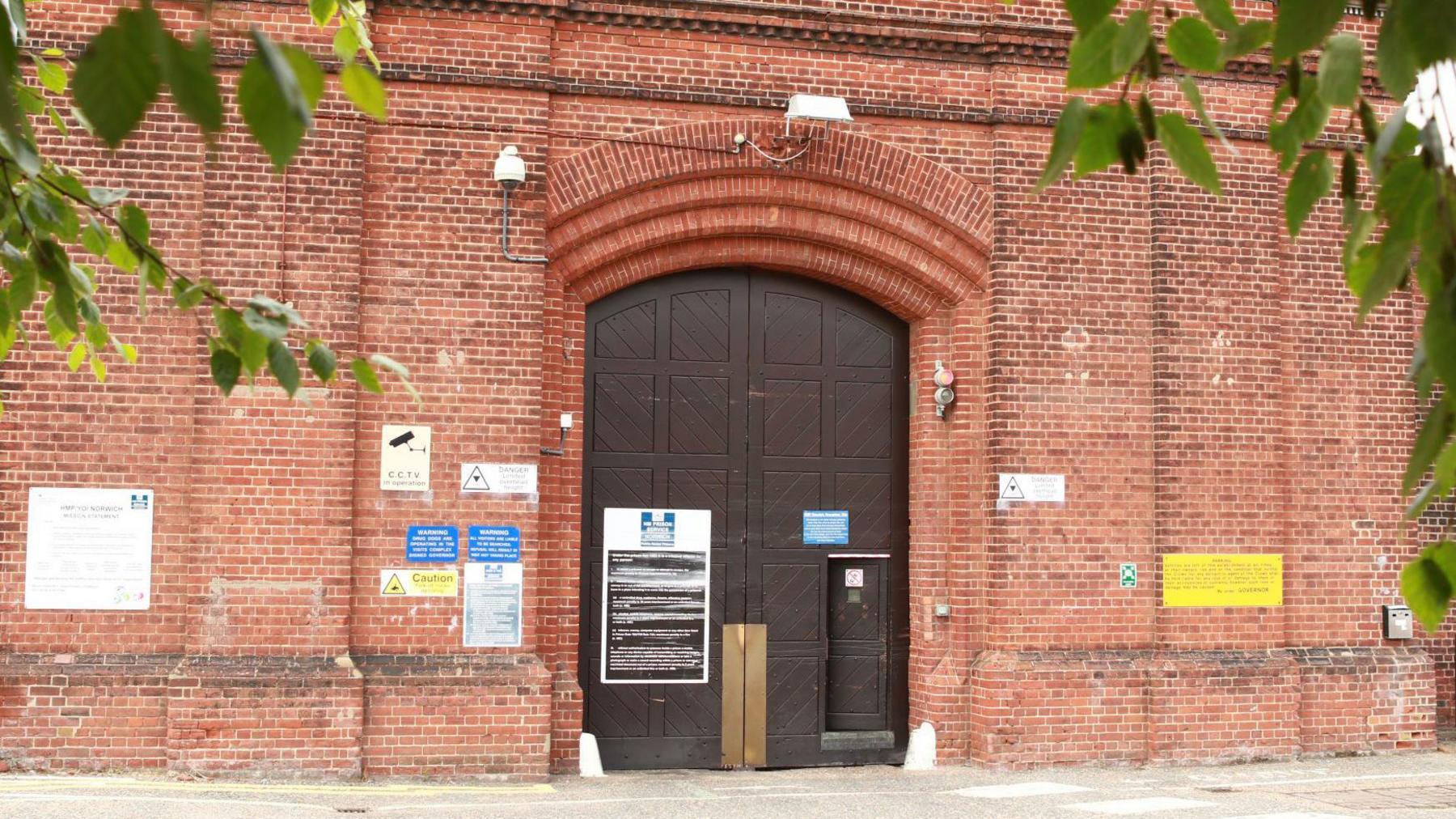 Exterior of Norwich jail. Brick building with a large wooden door and signage indicating the jail. 